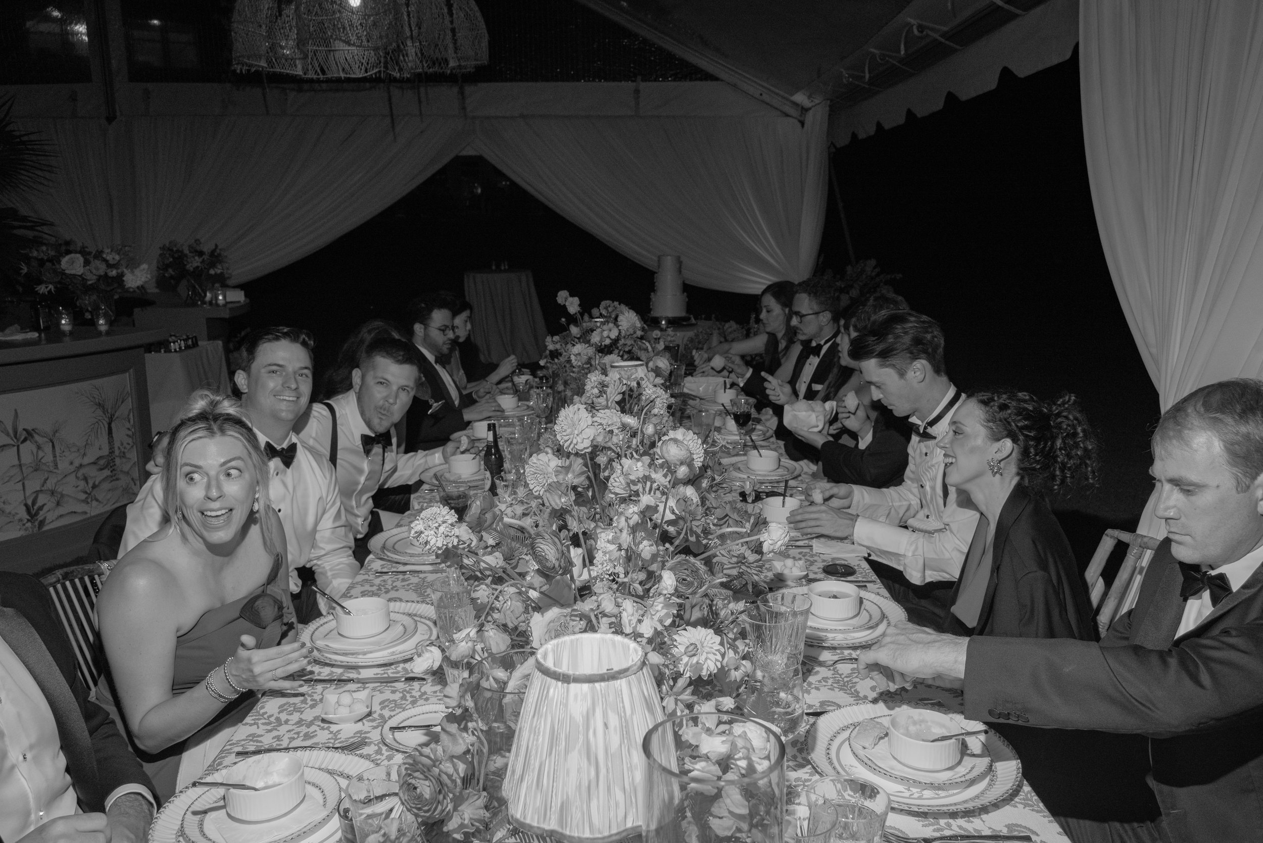 Black-and-white photograph of guests laughing around the long reception table during dinner.
