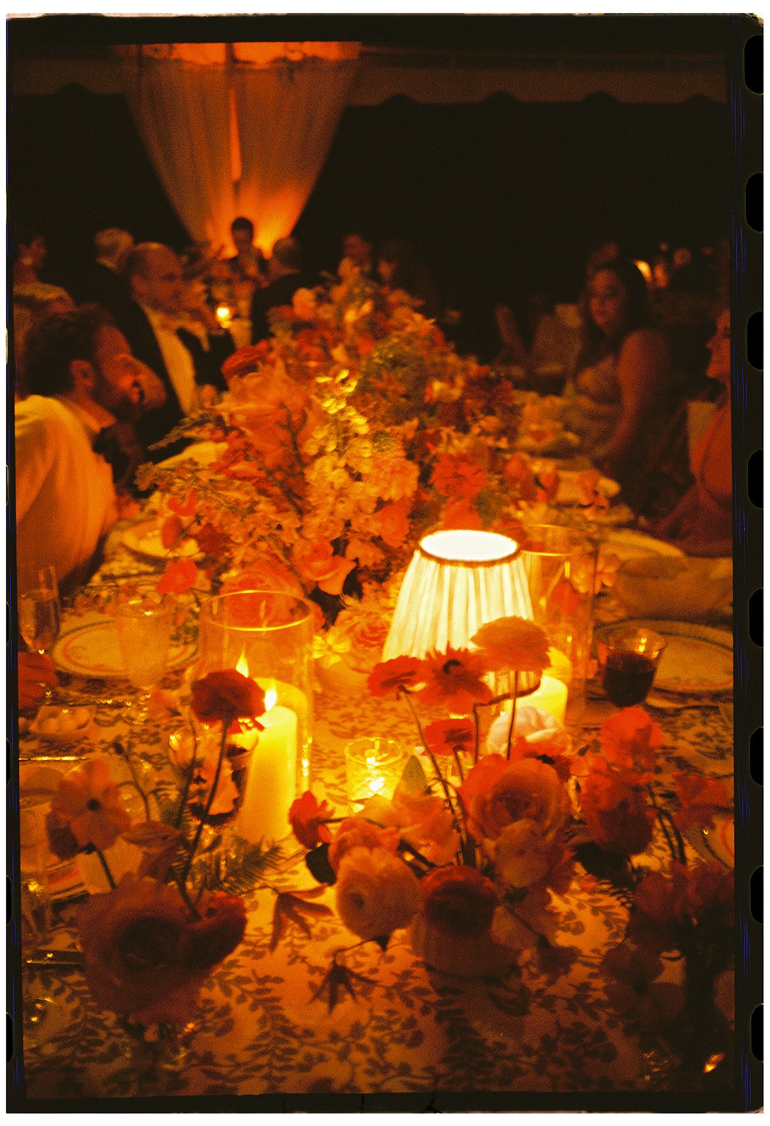 Candlelit wedding reception table with layered floral arrangements and warm evening lighting, showcasing intentional event design and atmosphere, photographed on 35mm film. 
