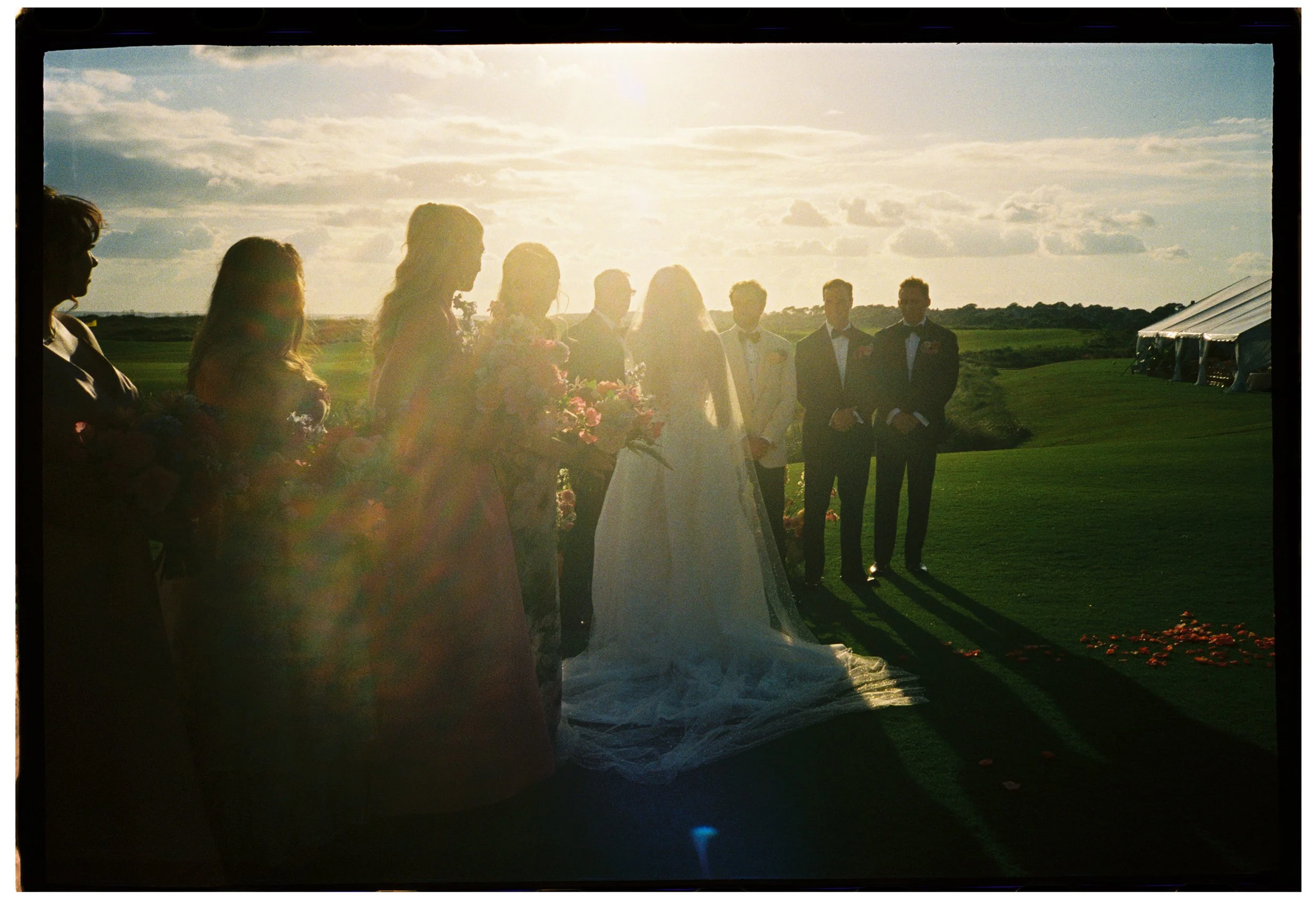 Film photograph of the wedding party gathered around Katie and Trevor in golden backlight during their Ocean Course ceremony.