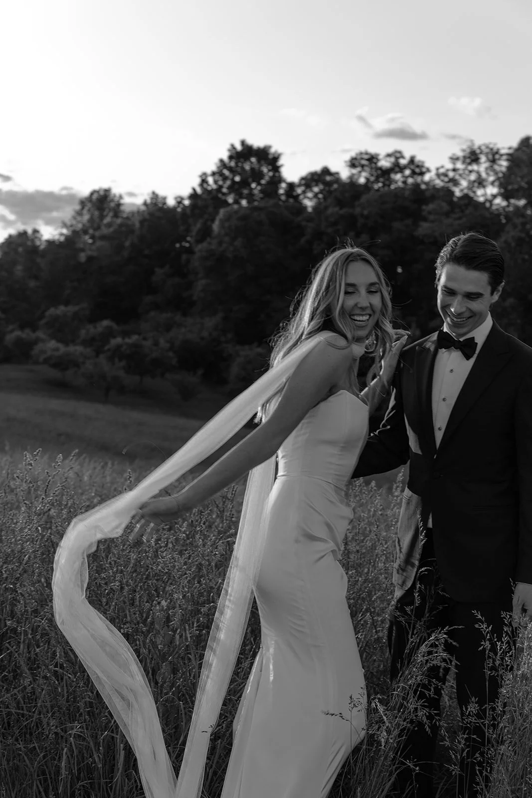 Black-and-white portrait of the bride walking through the Hayfield at Goodstone Inn with her long scarf-veil trailing behind her.