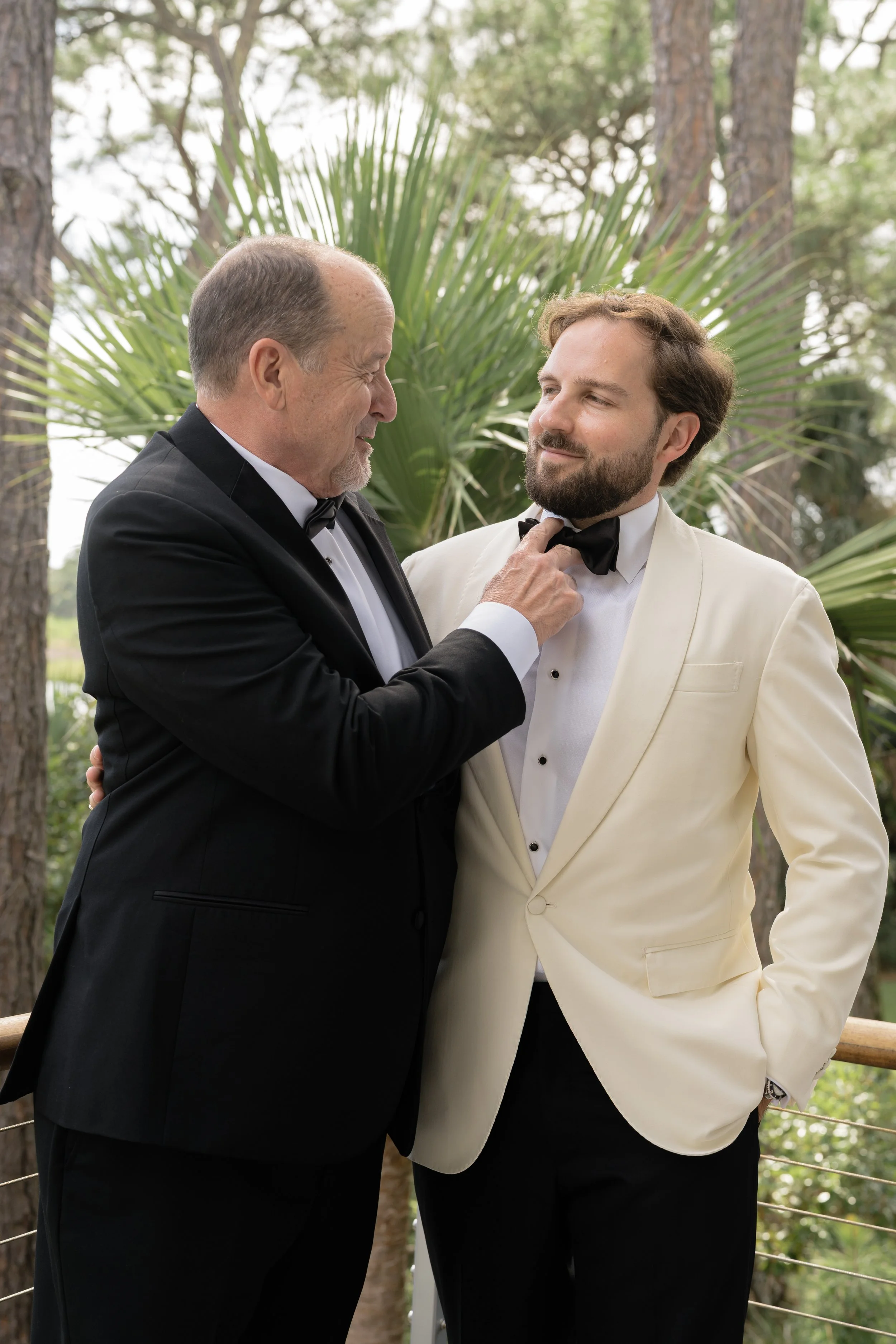 Trevor’s father adjusts his black bow tie as Trevor prepares in a white dinner jacket before the wedding ceremony.