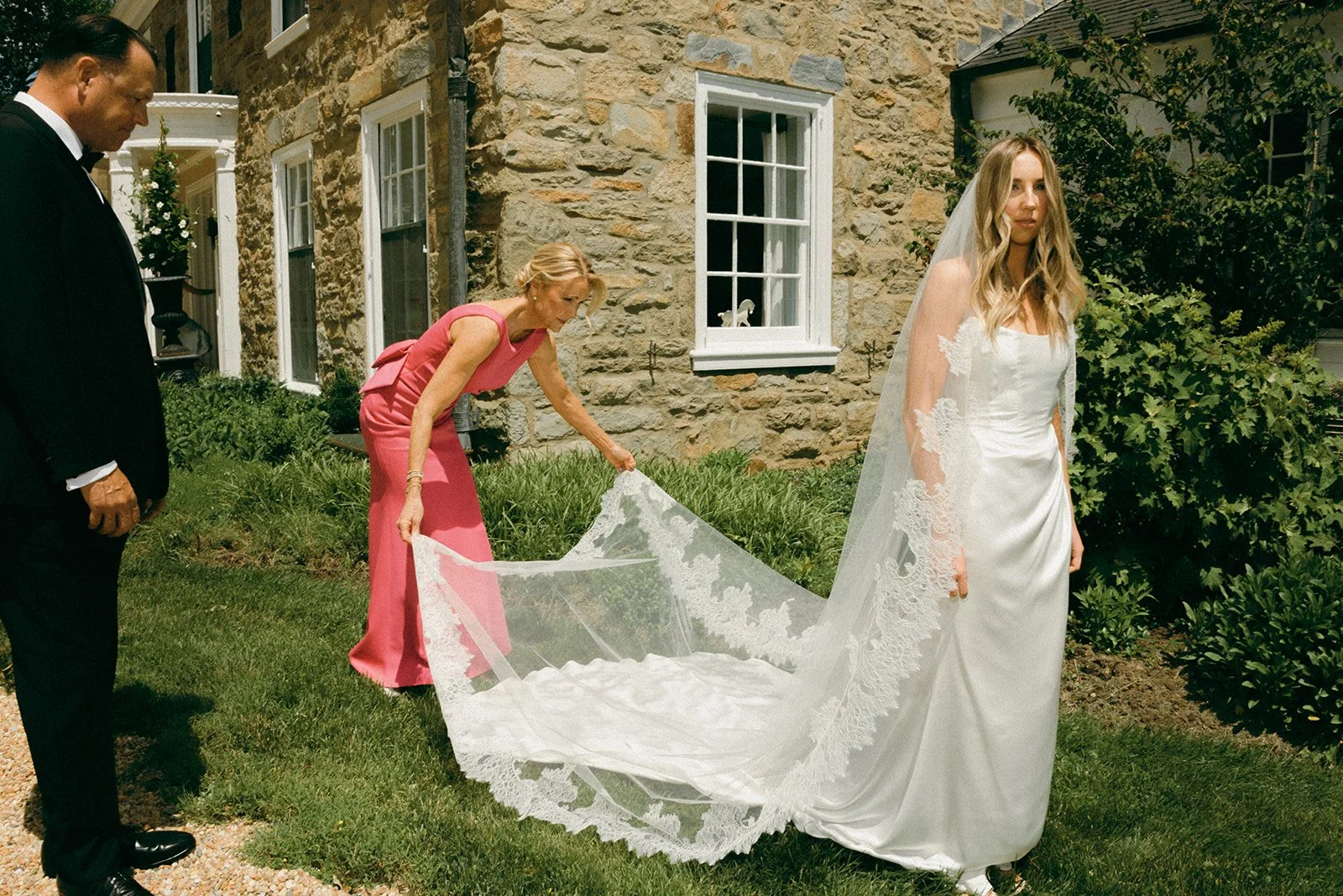 Bride's mother adjusts her train while they prepare for group photos at the Manor House