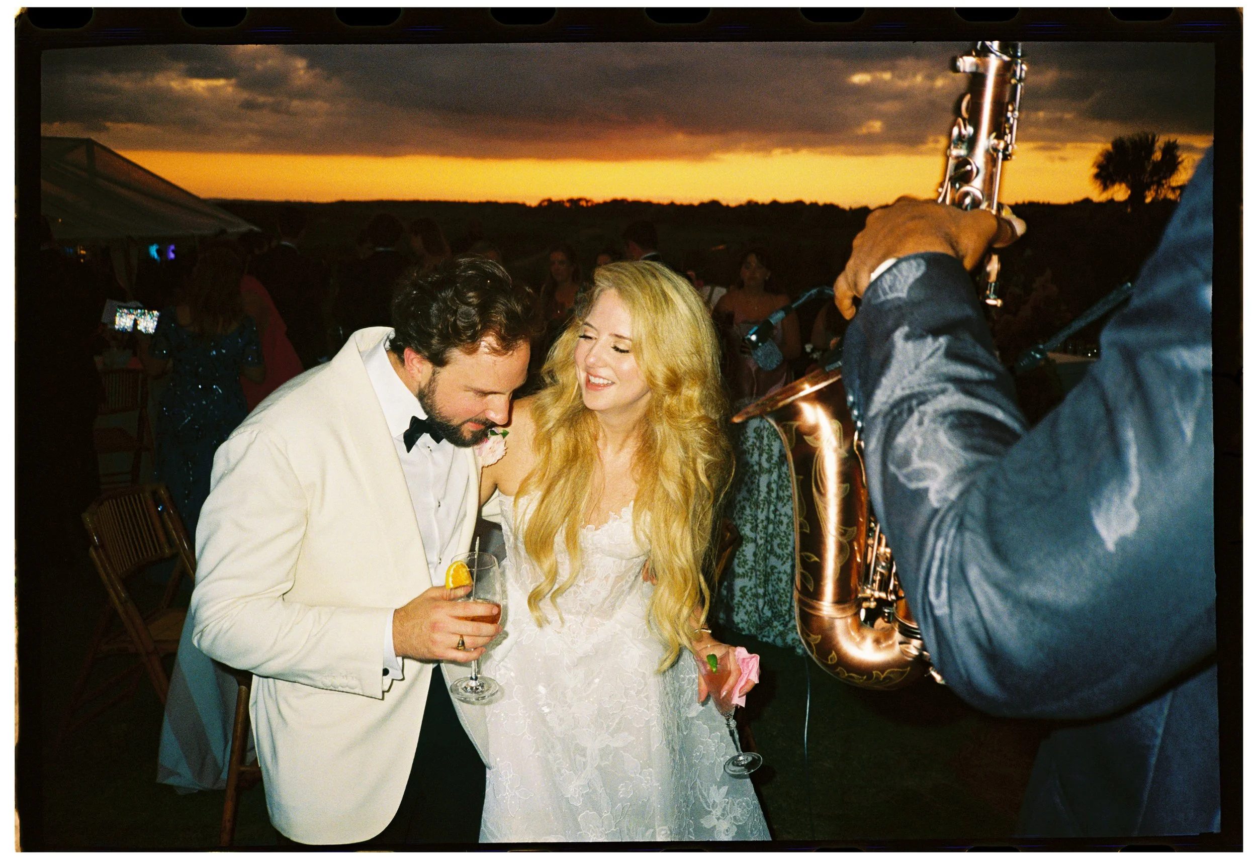 Katie and Trevor laugh together beside the saxophonist during the lively sunset cocktail hour at The Ocean Course.