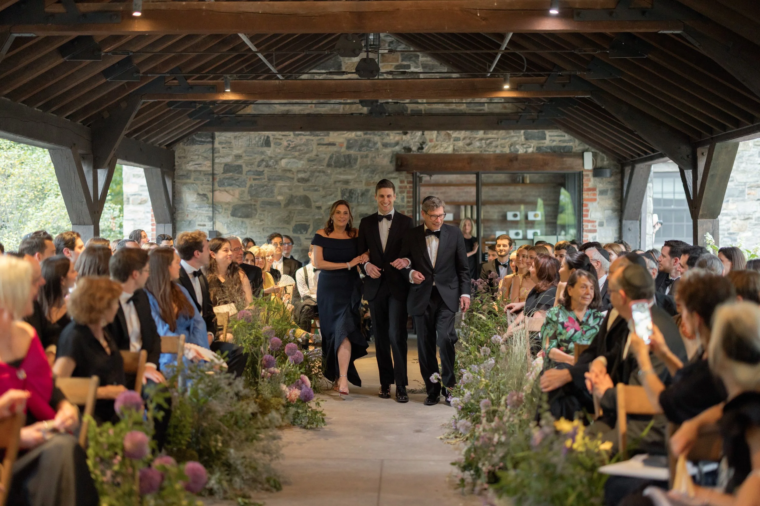 The groom makes his ceremony entrance and walks down the aisle with both his mother and father. 