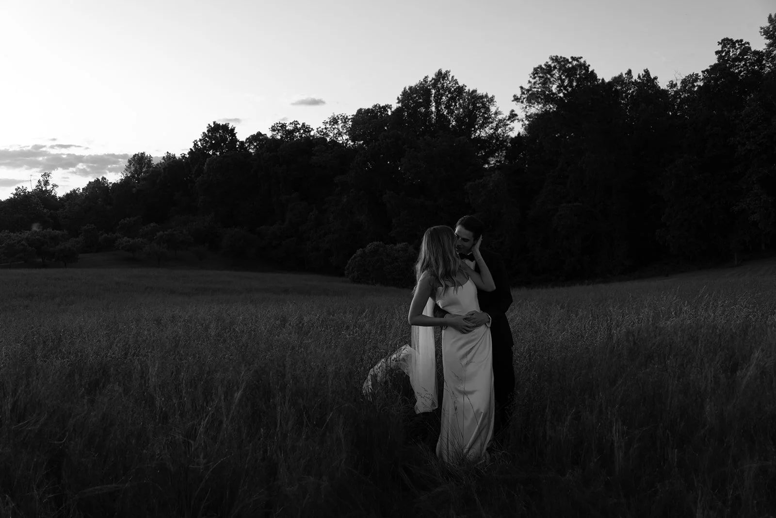 Black-and-white wide portrait of the bride and groom embracing in the Hayfield at Goodstone Inn.