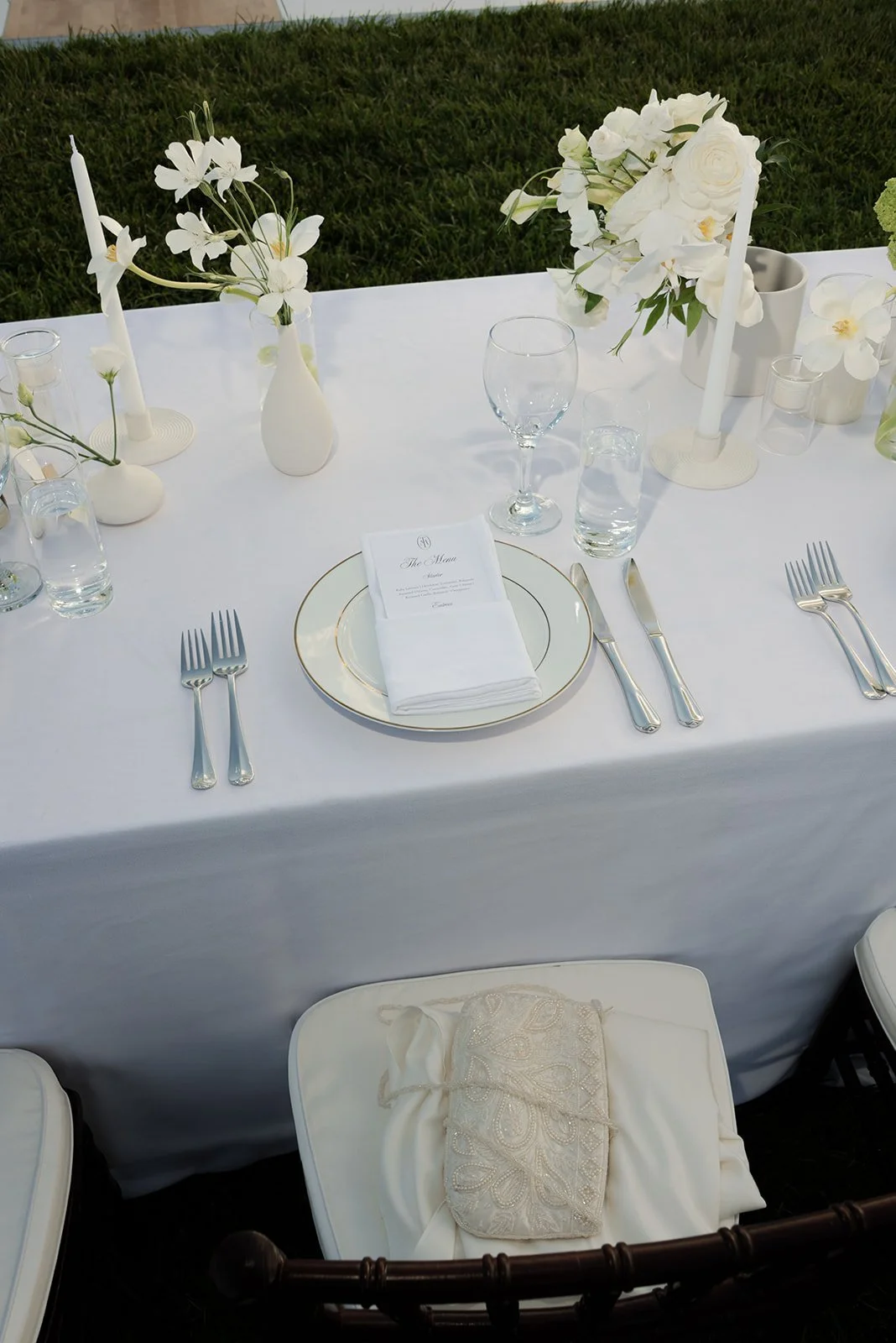 White linen reception place setting with candles, ivory flowers, and the bride's vintage beaded handbag resting on her chiavari chair at Goodstone Inn