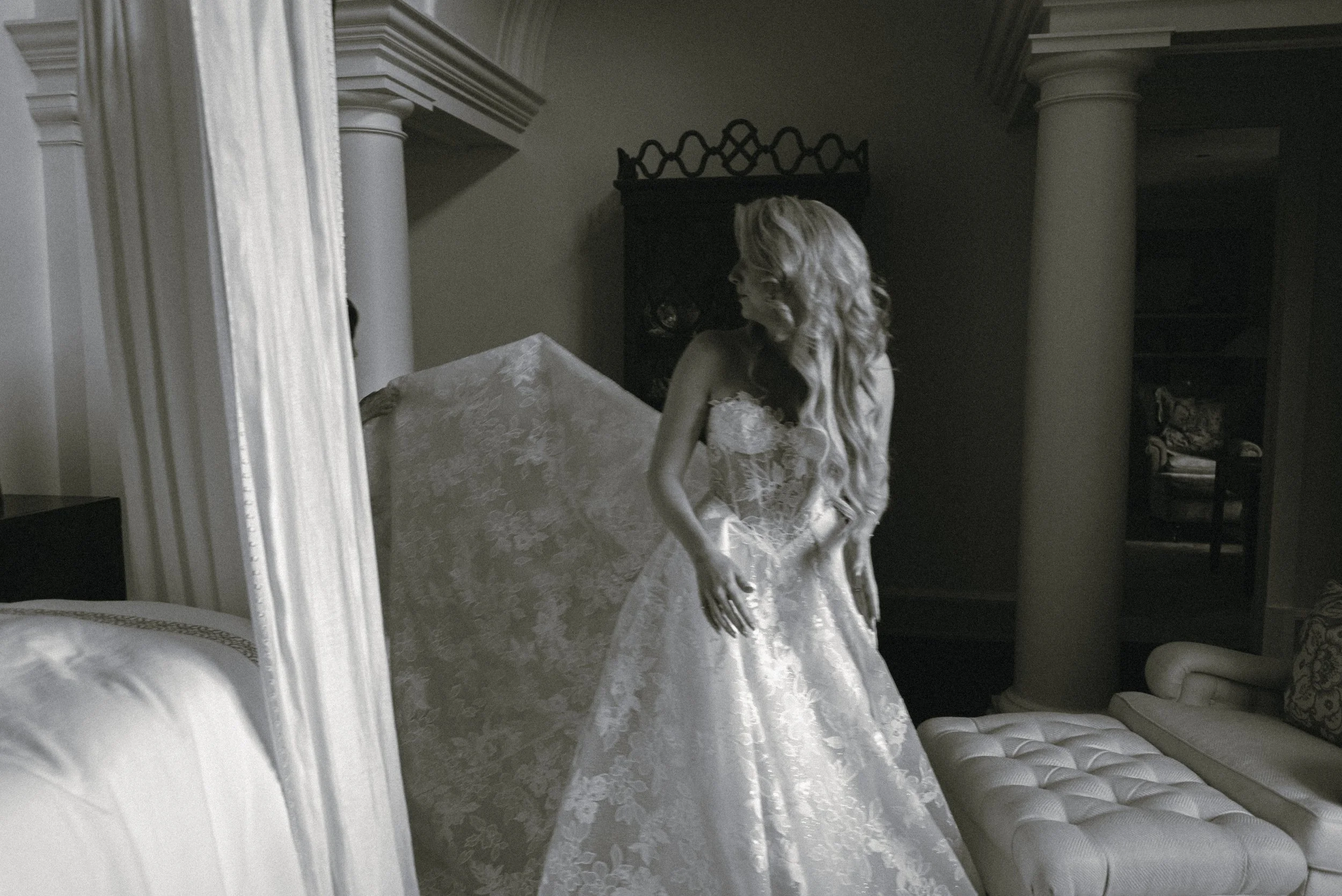 Black-and-white portrait of Katie holding the full skirt of her lace Galia Lahav wedding gown inside the private Kiawah Island estate.