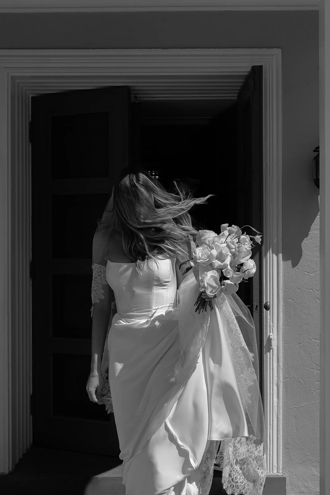 Black-and-white cinematic portrait of the bride in her wedding gown with the wind blowing her hair framed by an interior doorway at Goodstone Inn.
