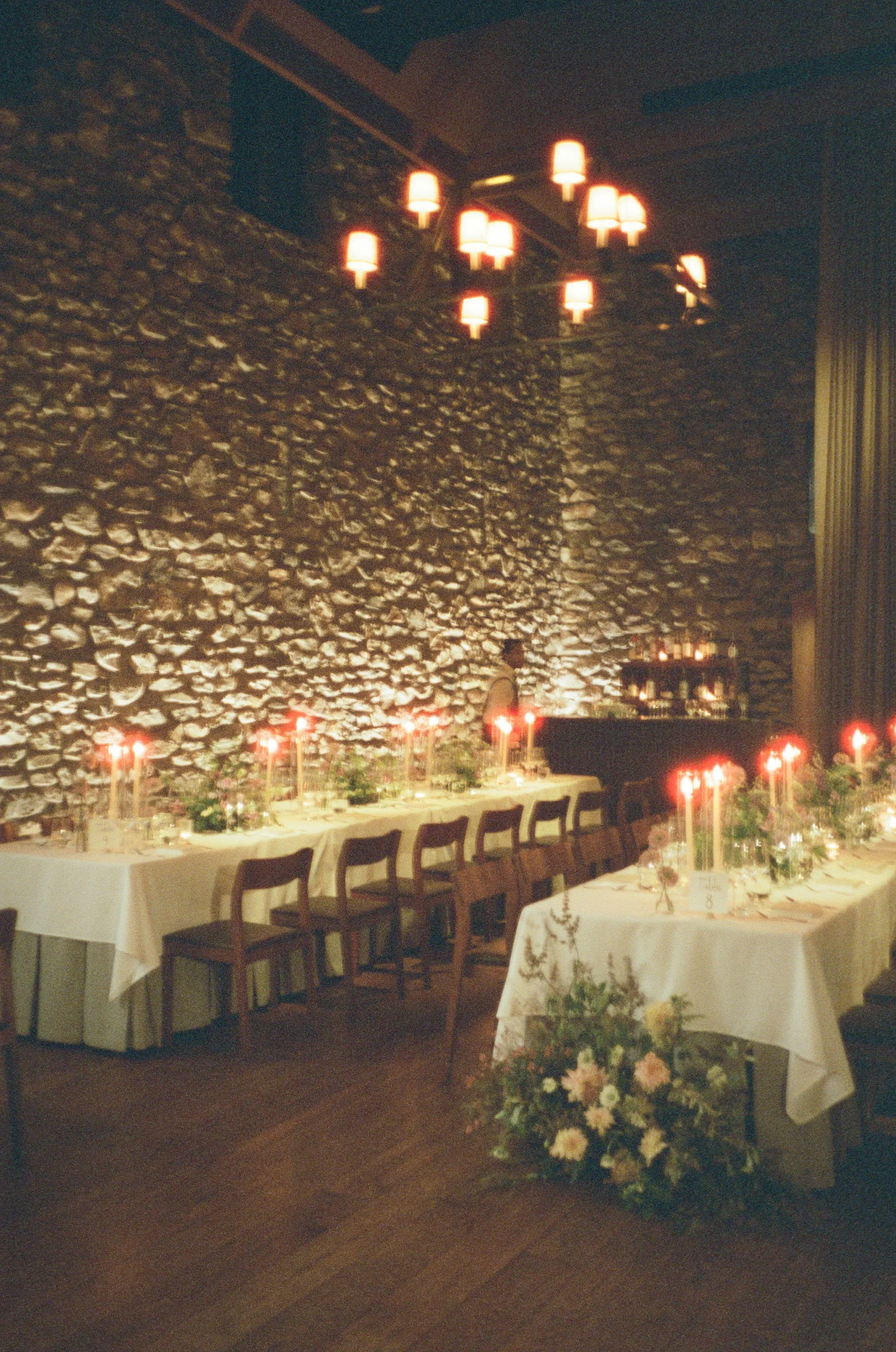 Film photograph of the candlelit reception dining room at Blue Hill at Stone Barns with long tables, florals and historic stone walls.