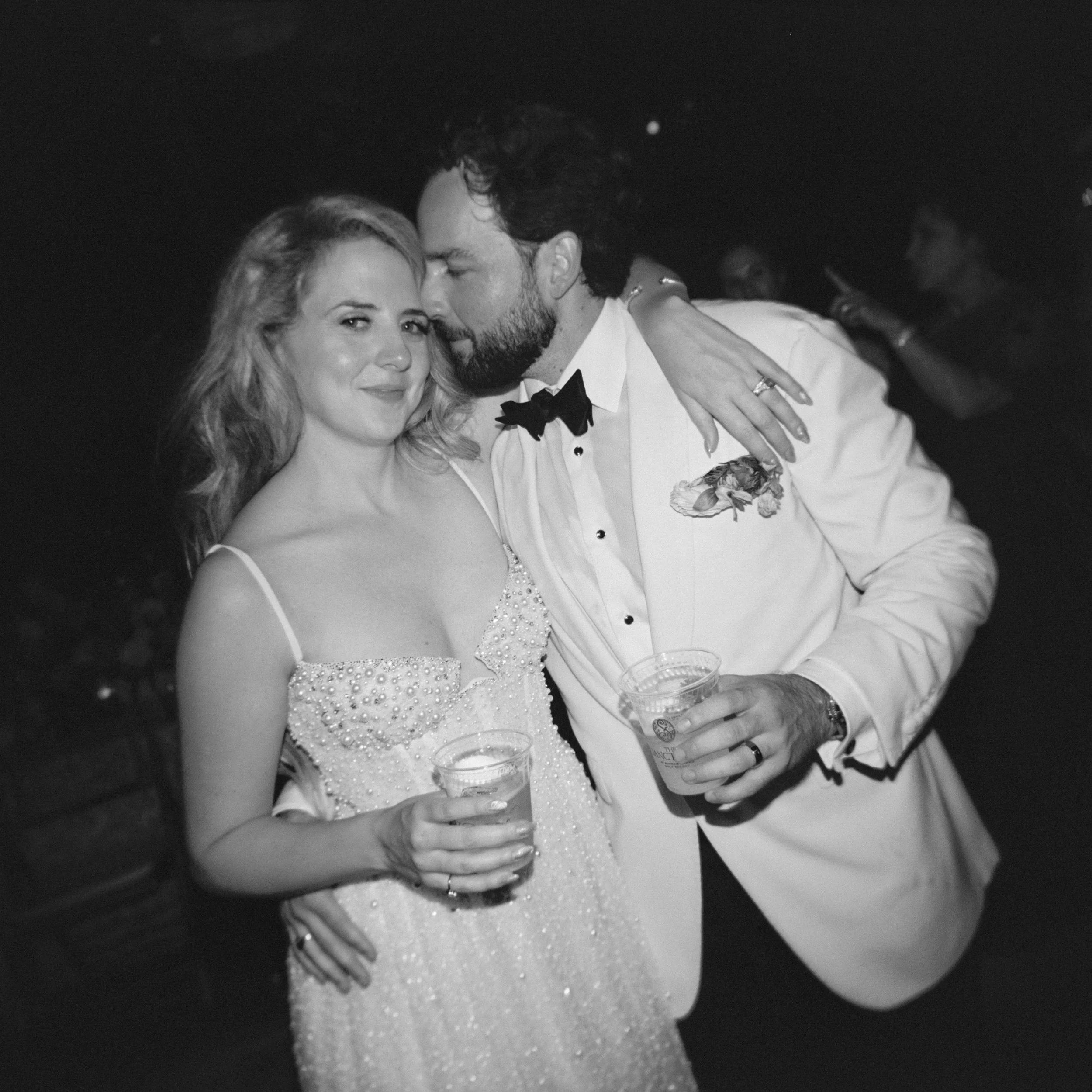 Black-and-white medium format film photograph of Katie holding a cocktail as Trevor leans close during the reception.