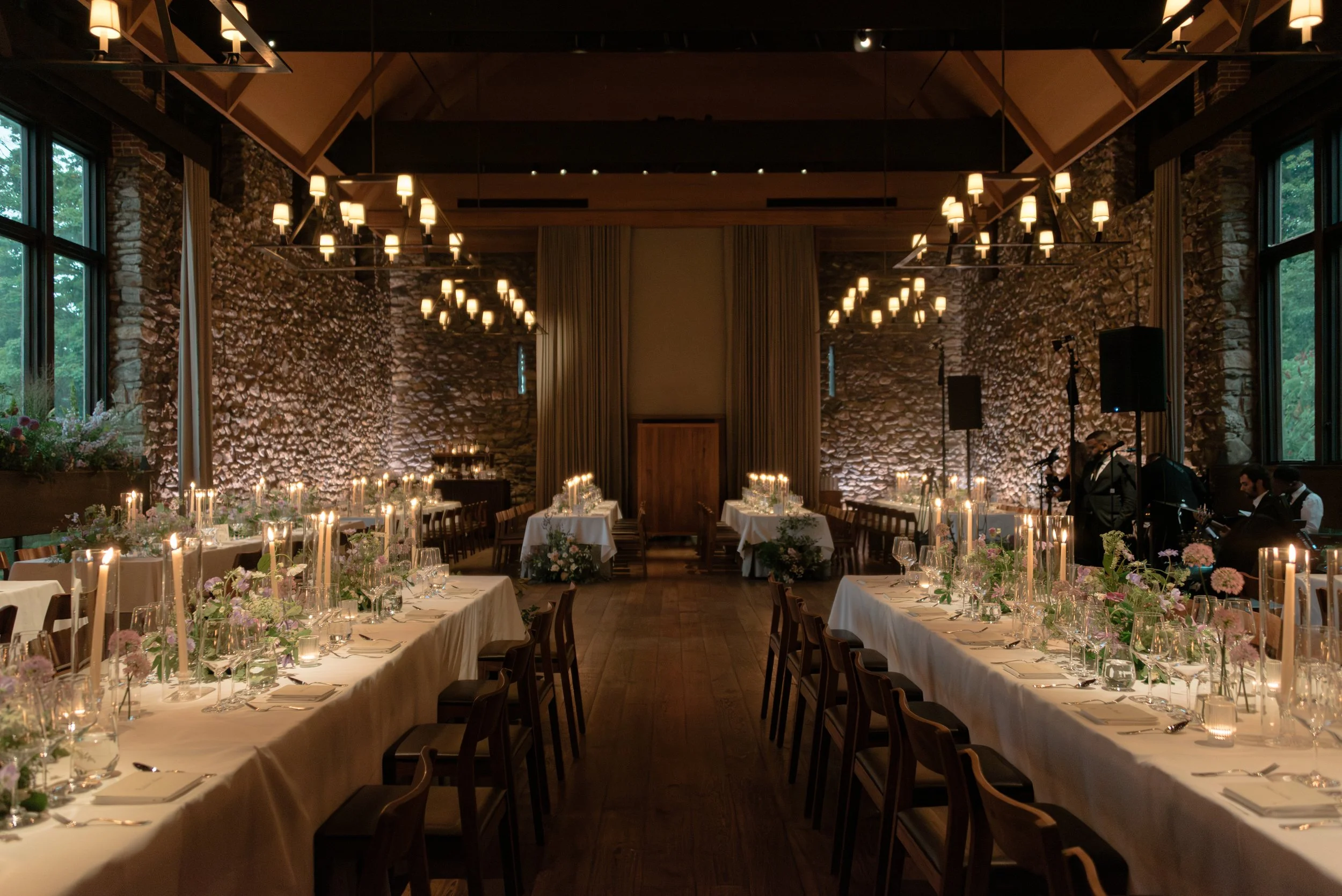 Wide view of Jennie and Will’s Blue Hill at Stone Barns reception with parallel dinner tables, candlelight and floral design.