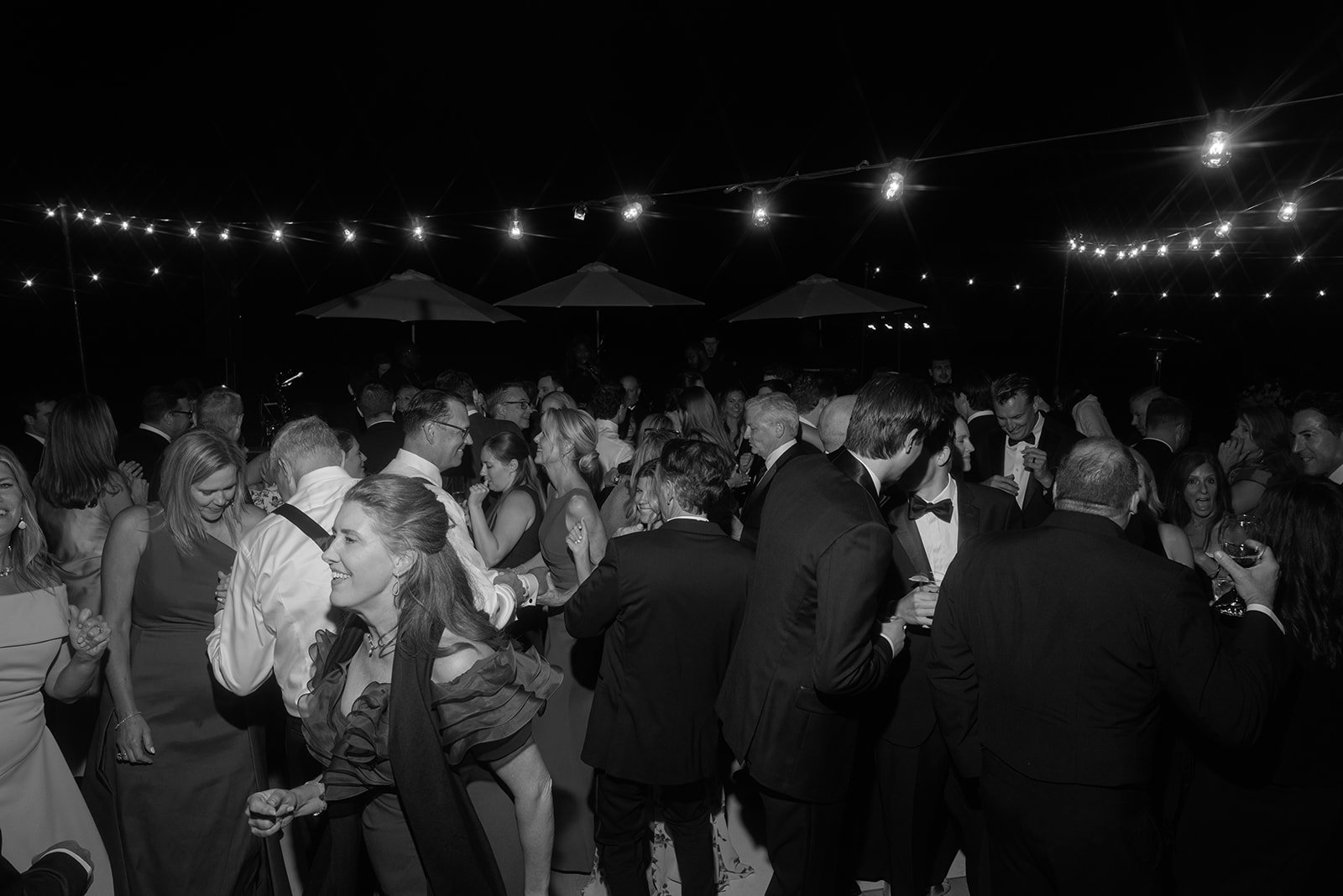 Black-and-white documentary photograph of wedding guests dancing beneath string lights during an outdoor reception at Goodstone Inn.