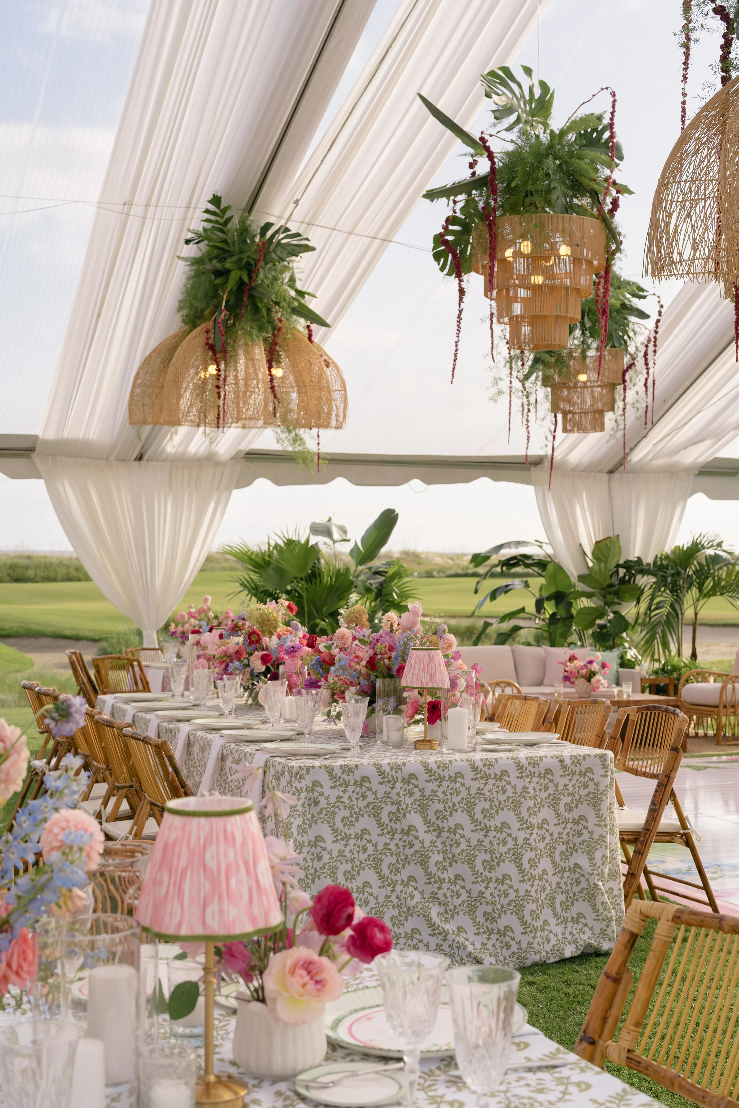 Clear-top reception tent filled with colorful flowers, patterned linens, rattan chairs, and woven chandeliers at The Ocean Course on Kiawah Island.