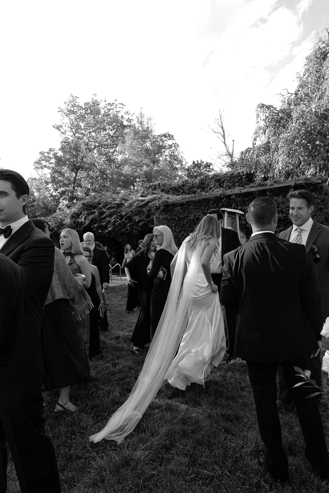 Black-and-white photograph of the bride walking through the crowd of guests during cocktail hour around the pool terrace at Goodstone Inn