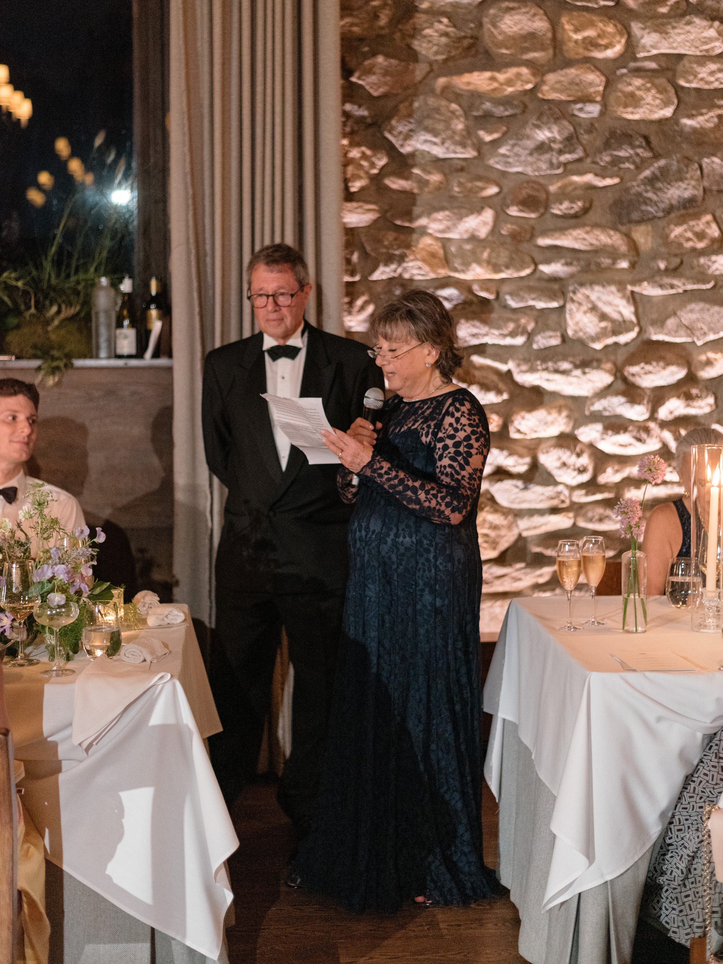 The bride's mom speaking beside Jennie and Will during the candlelit wedding dinner.