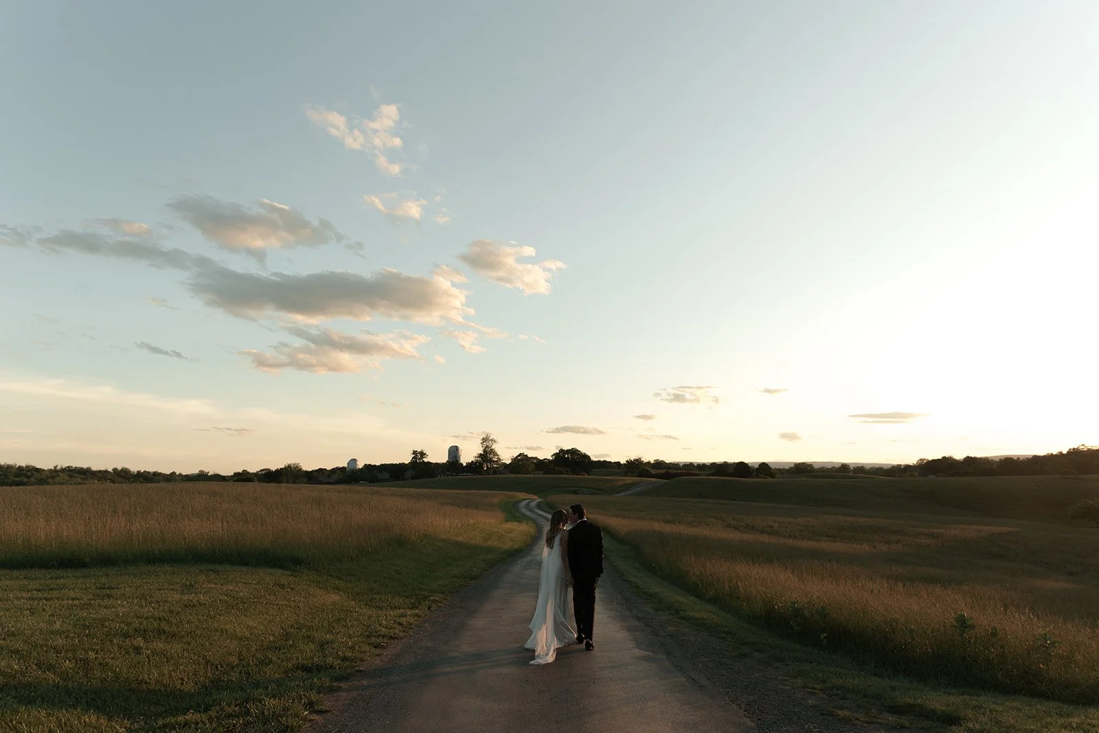 Bride and groom standing in the Hayfield at sunset at Goodstone Inn beneath a softly colored sky.