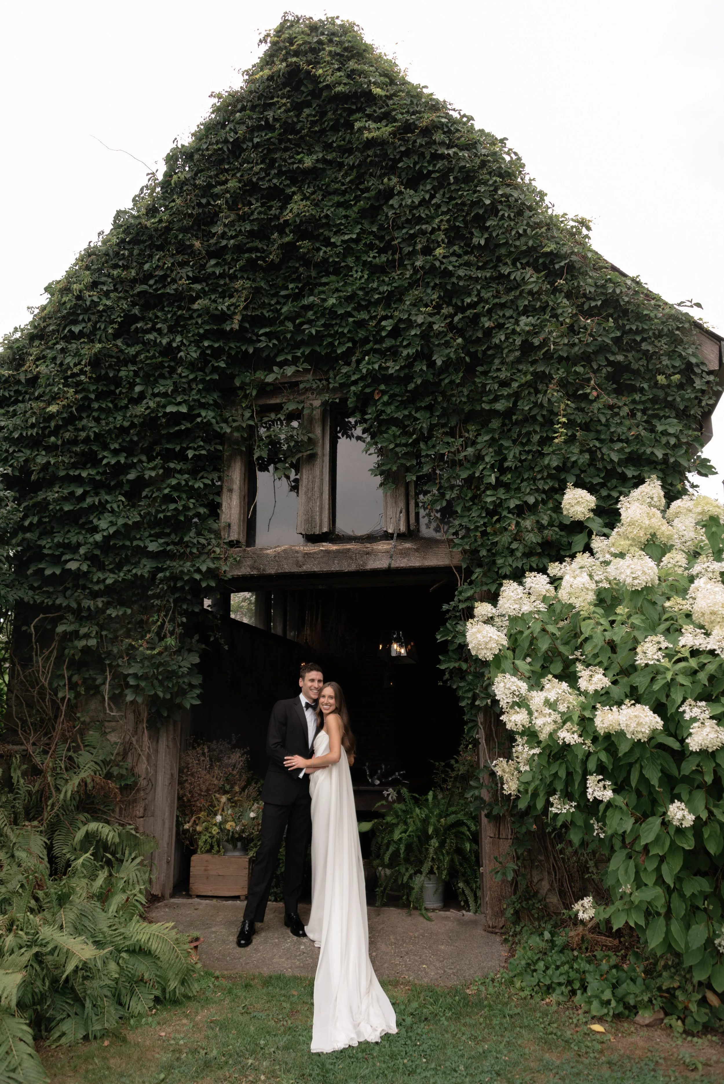 Newlywed couple standing beneath lush greenery at Blue Hill at Stone Barns in Tarrytown, New York, photographed with a timeless editorial approach to destination wedding storytelling.