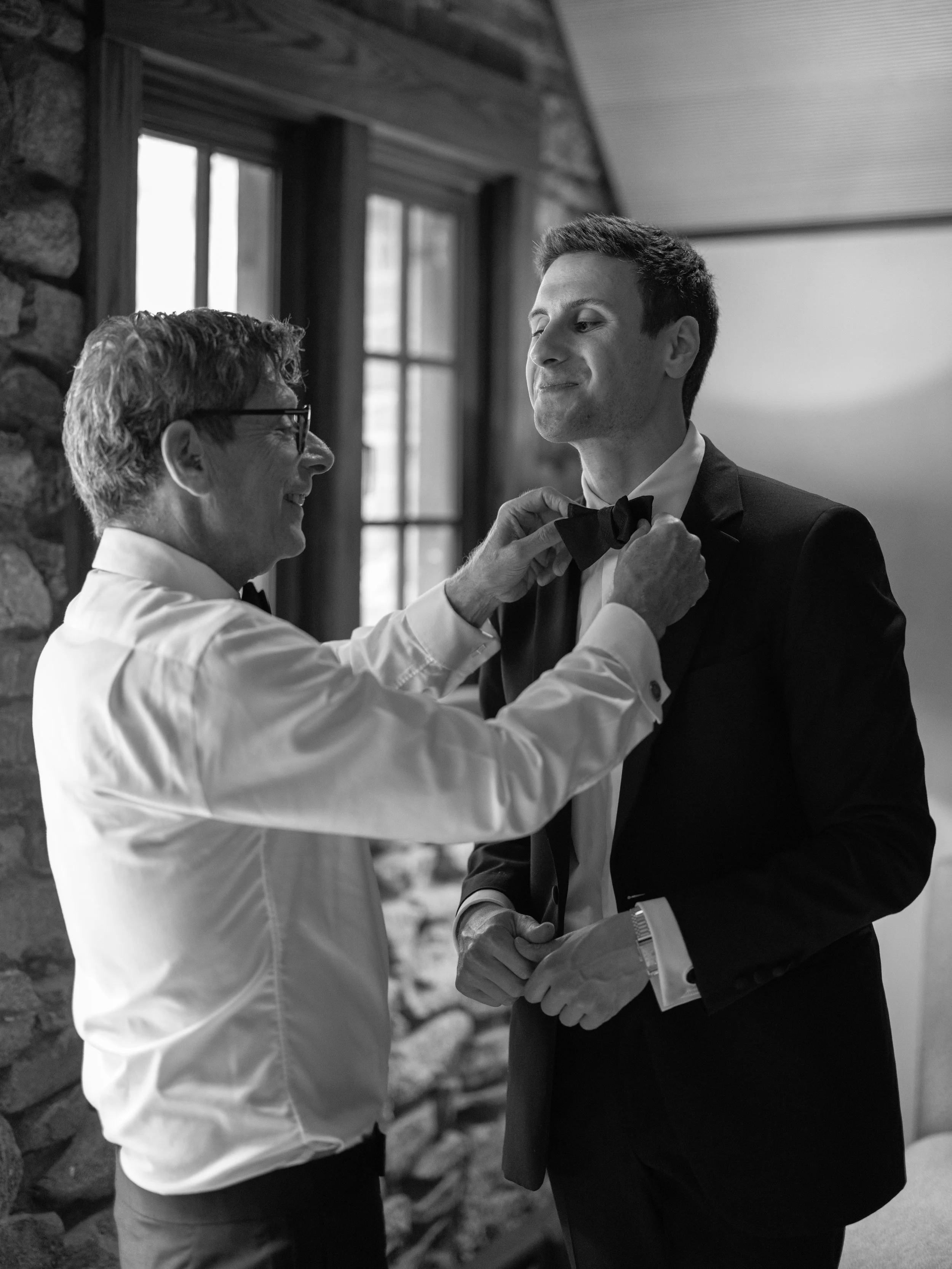 The groom's father straightens his bow tie while he gets ready before the wedding ceremony.