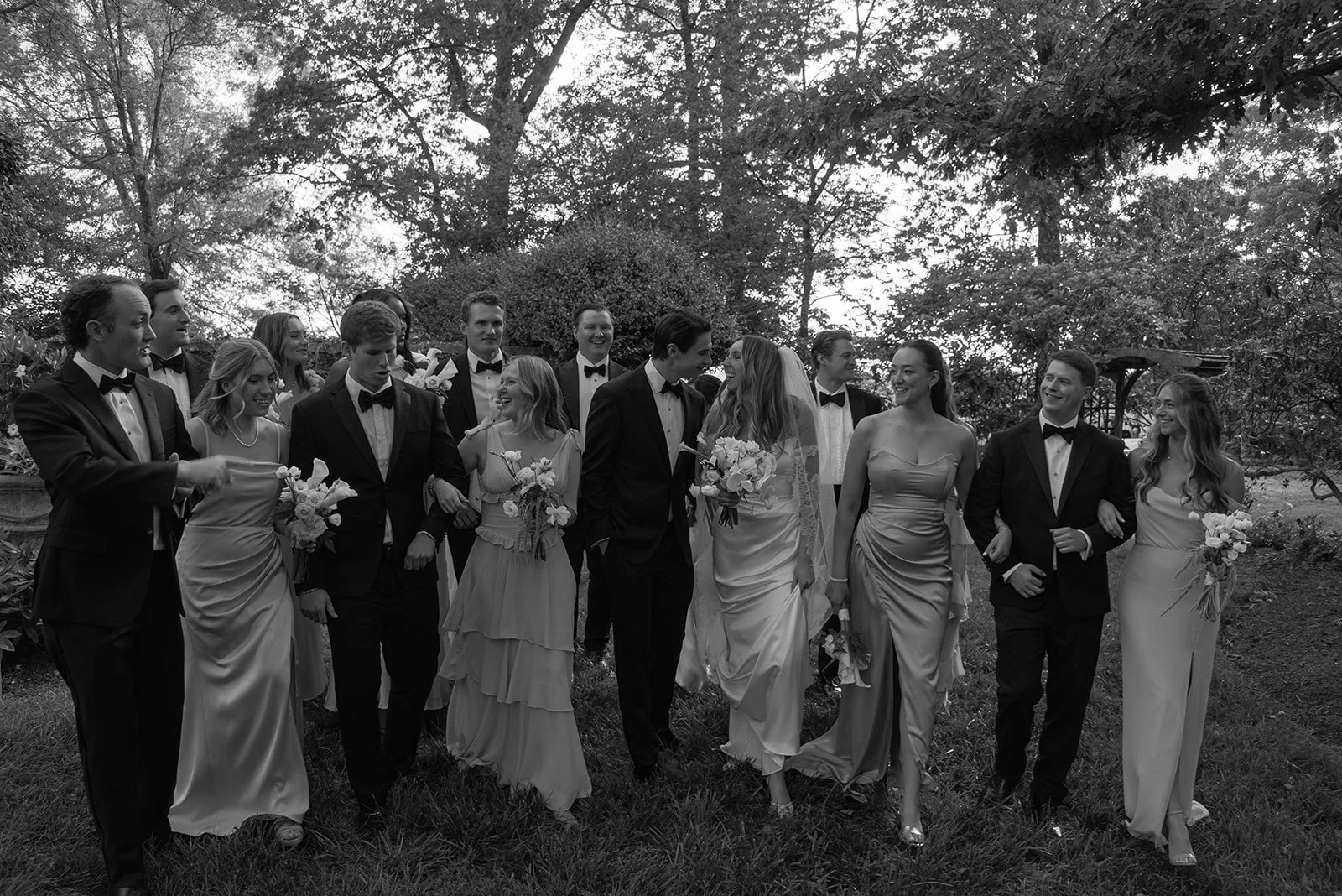 Black-and-white group portrait of bridesmaids and wedding guests outdoors beneath trees at Goodstone Inn.