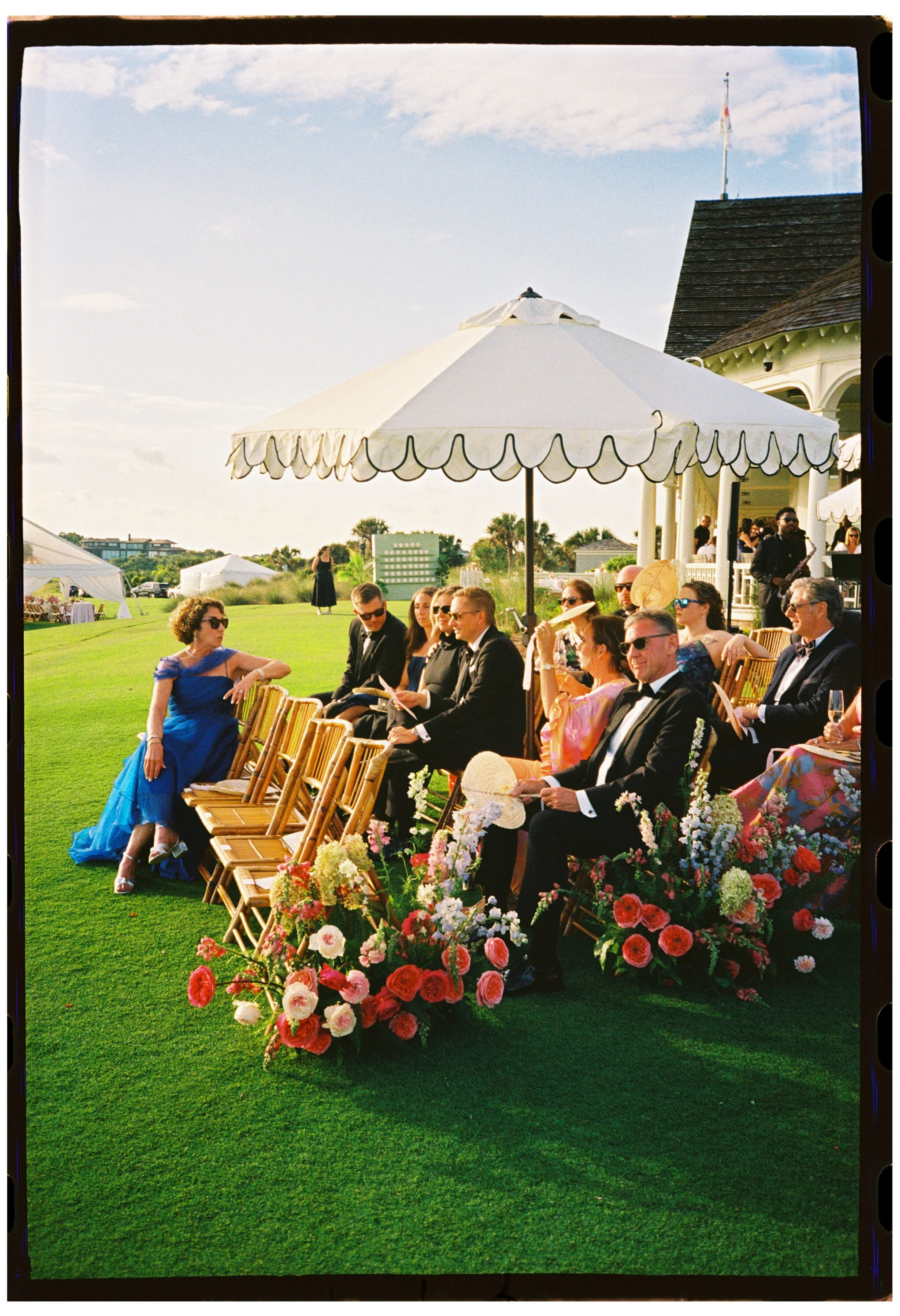 Guests gather among colorful aisle flowers before the outdoor wedding ceremony at The Ocean Course on Kiawah Island, shot on 35mm film photography.