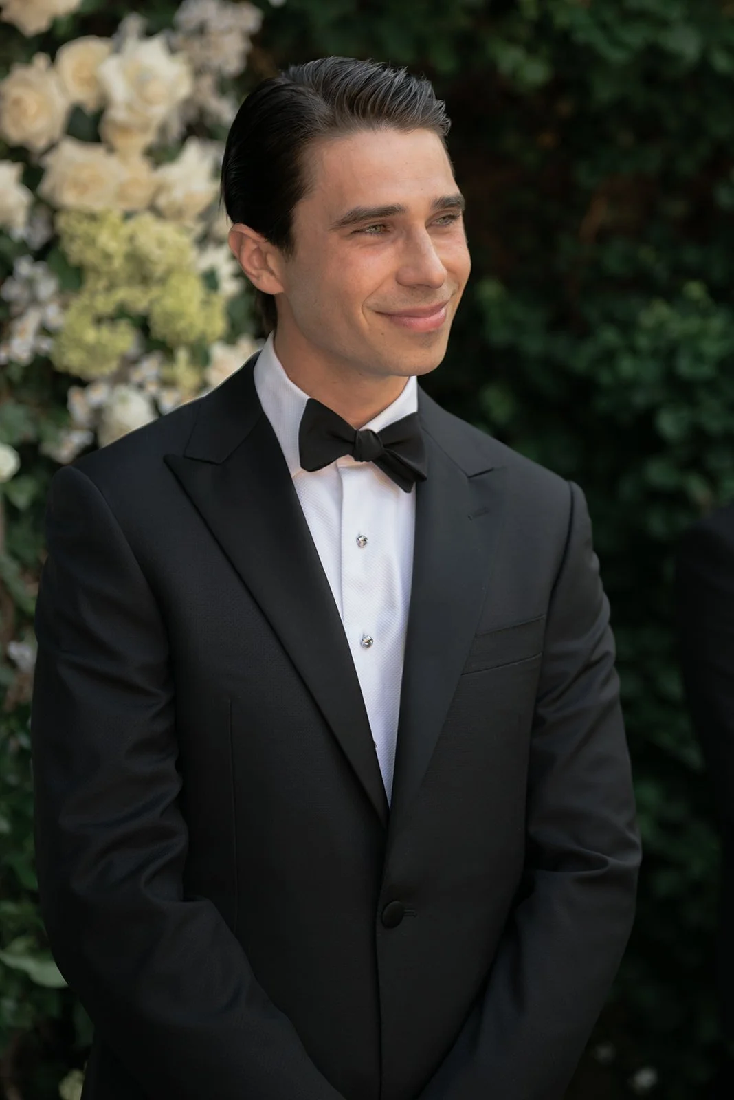 Groom smiling during the outdoor ceremony at Goodstone Inn with white flowers and greenery behind him.