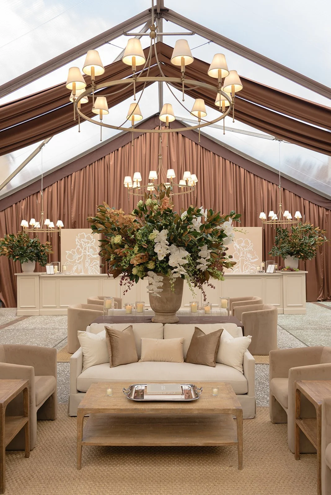 Elegant sailcloth wedding tent interior with layered chandeliers, neutral lounge furniture, and a large floral installation inspired by Ralph Lauren Low-Country aesthetic..