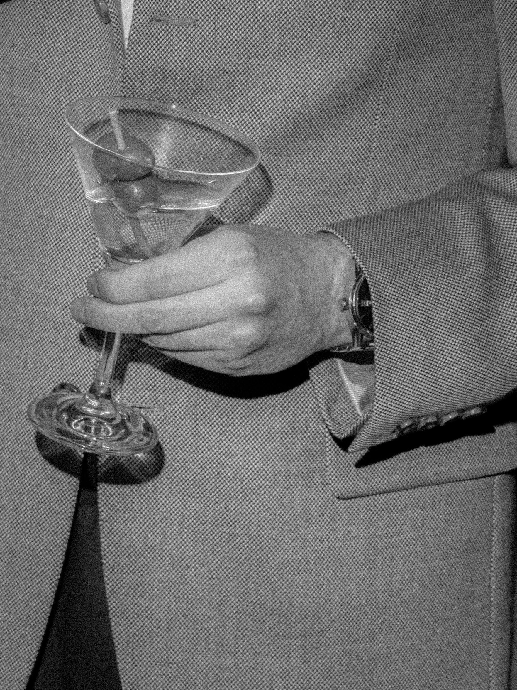 Black-and-white close-up of a martini glass held during cocktail hour at the rehearsal dinner.