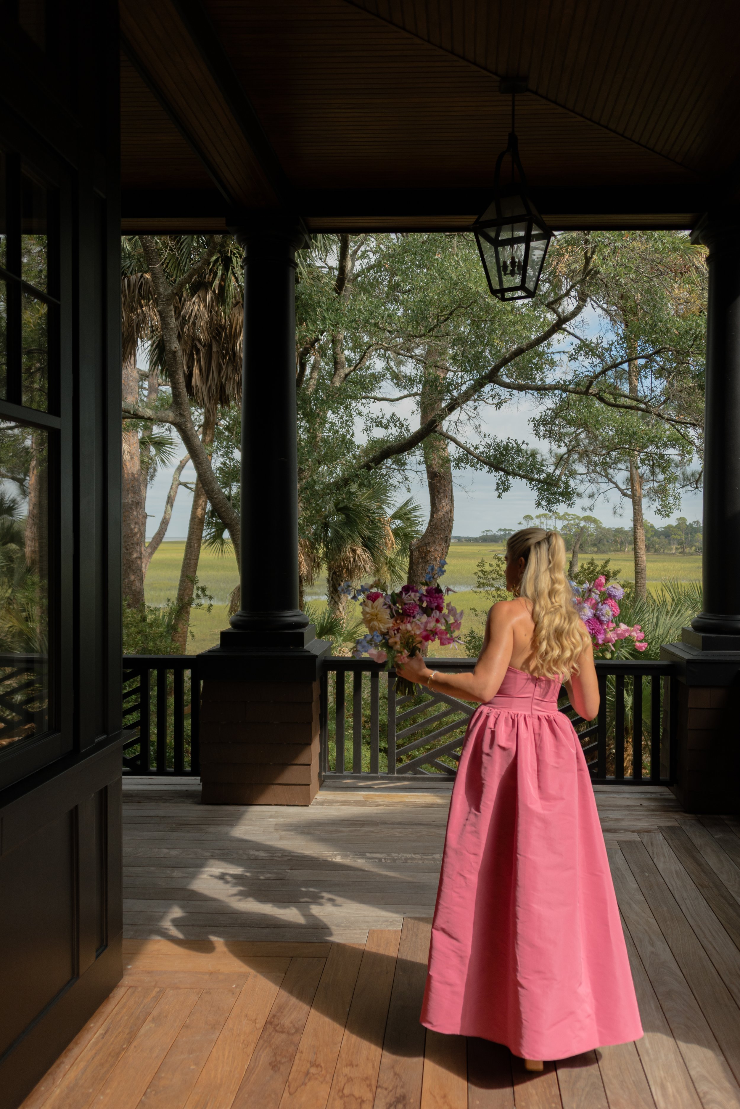 Maid of Honor in a vivid pink gown stands on the shaded porch of the private coastal estate on Kiawah Island.