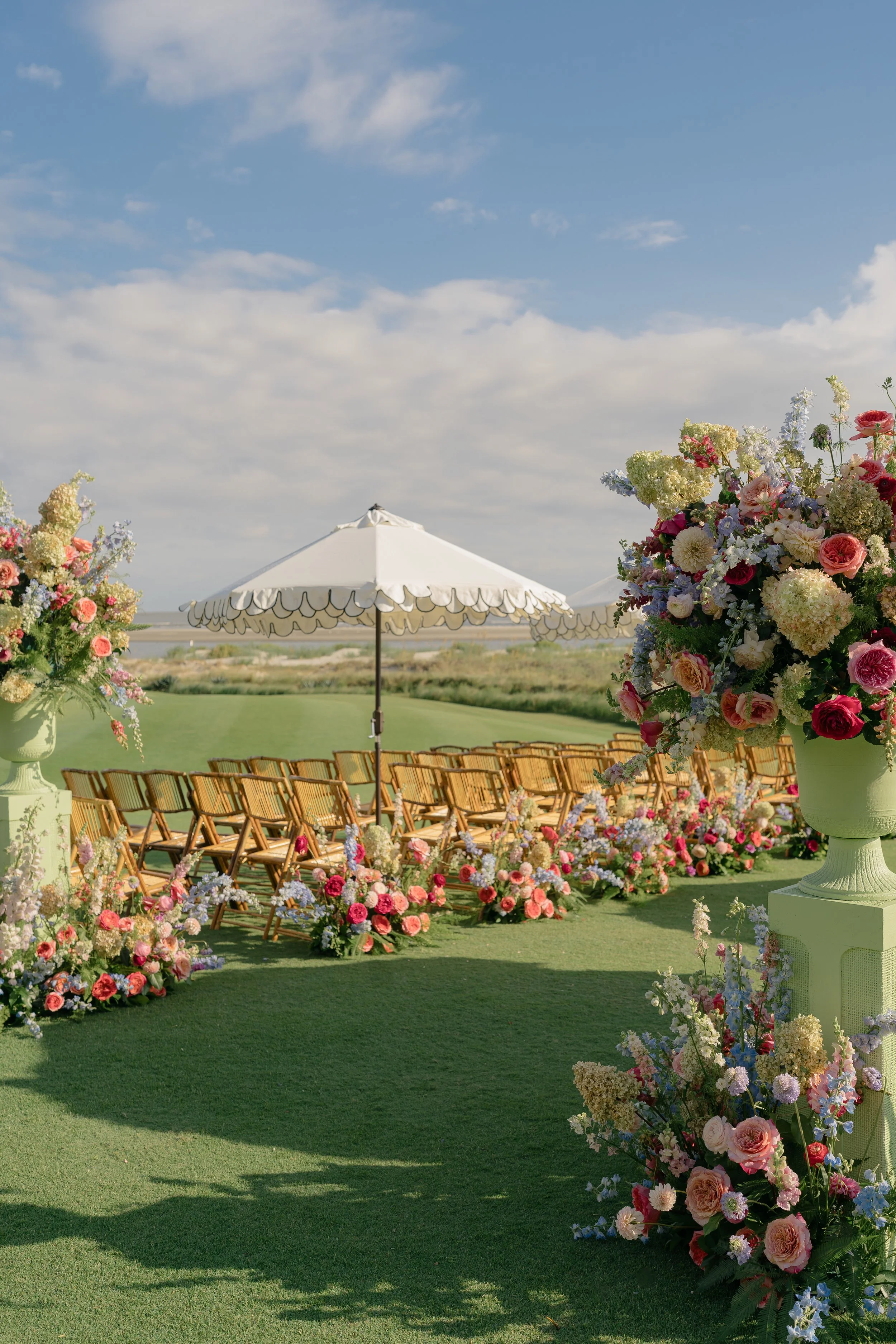 Colorful wedding ceremony overlooking the Atlantic Ocean at The Ocean Course on Kiawah Island, with abundant aisle flowers and urn arrangements by Festoon.