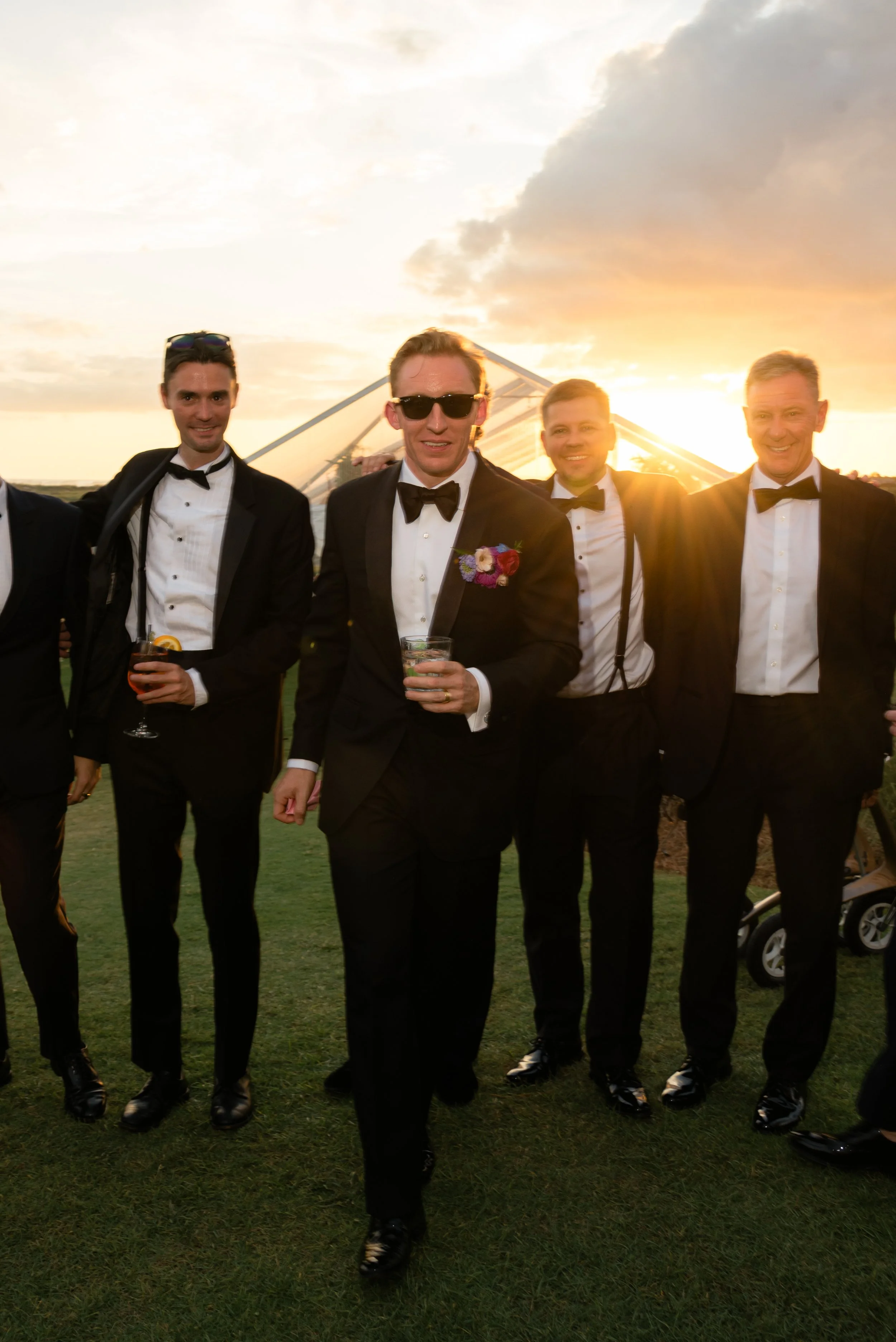 Trevor’s groomsmen walk together across the Ocean Course lawn in black-tie attire at sunset.