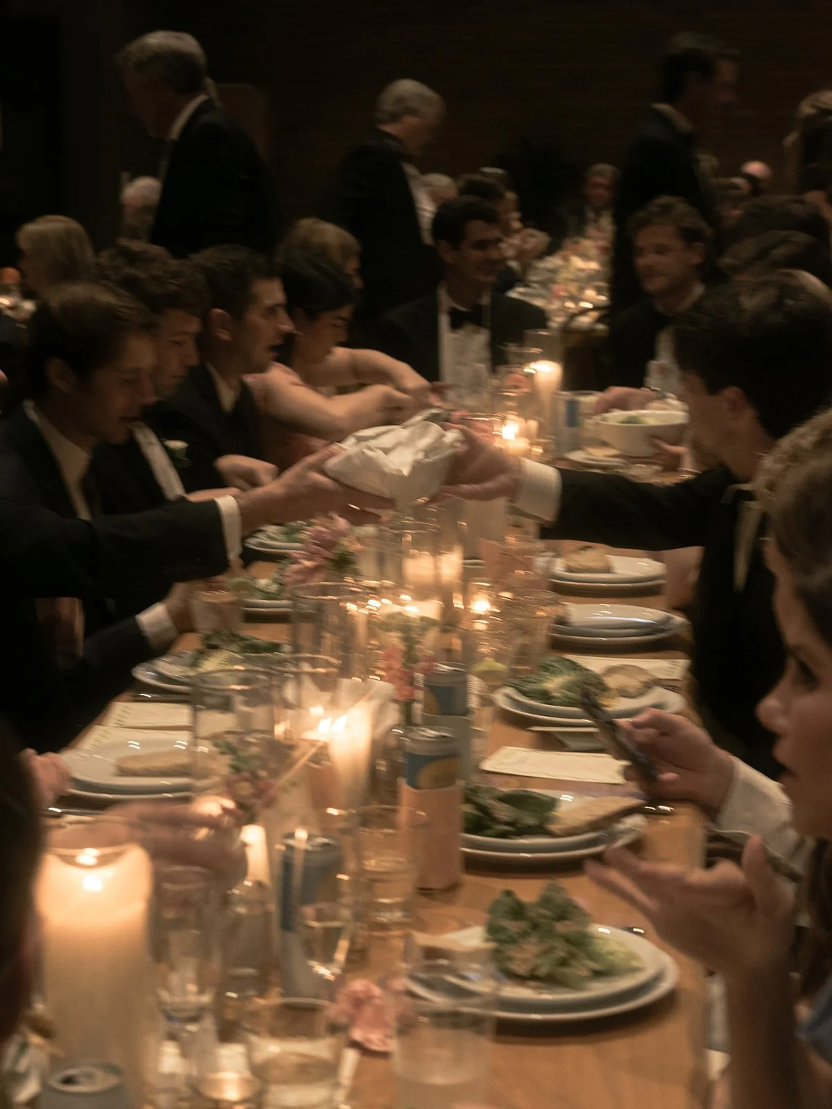 Wedding guests gathered around a long candlelit dinner table in an intimate reception setting.