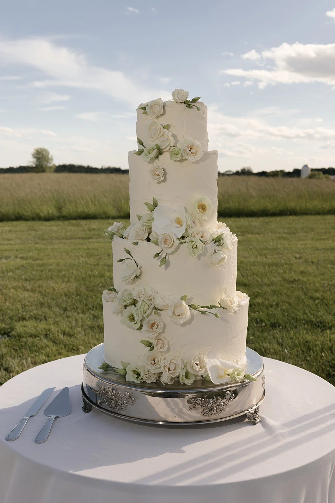 White tiered wedding cake decorated with delicate flowers against the open fields at Goodstone Inn.