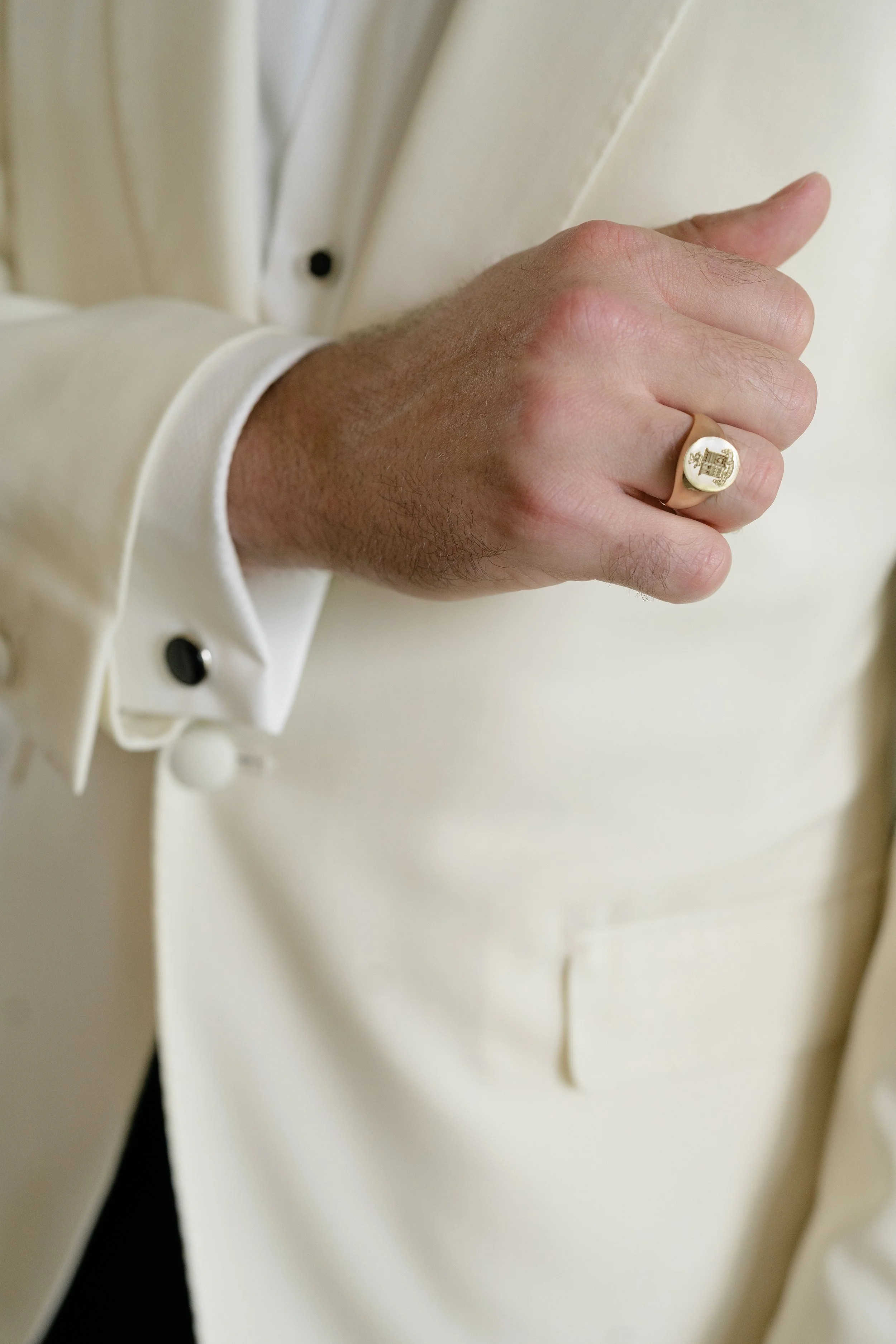 Close view of Trevor’s hand wearing a gold signet ring against the sleeve of his white dinner jacket.