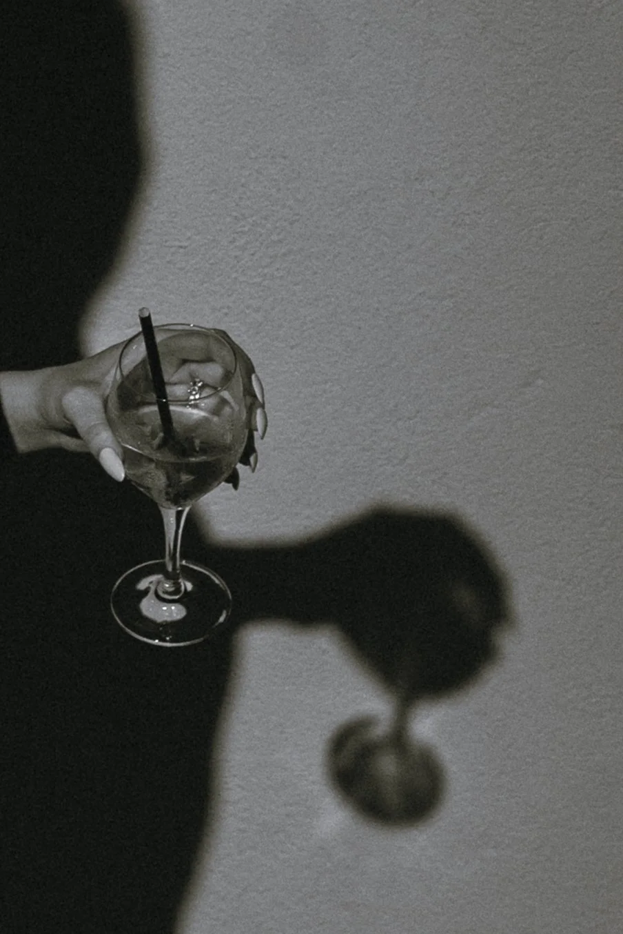 Black and white editorial photograph of a cocktail glass casting a shadow on a wall, highlighting atmosphere, design, and the art of gathering.
