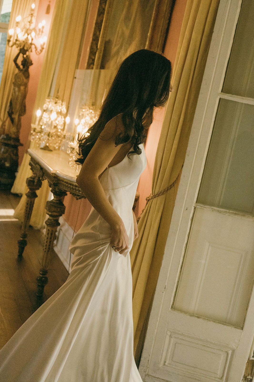 Film wedding photograph of a bride in a satin gown moving through the warmly lit historic interior of the William Aiken House in Charleston, SC.