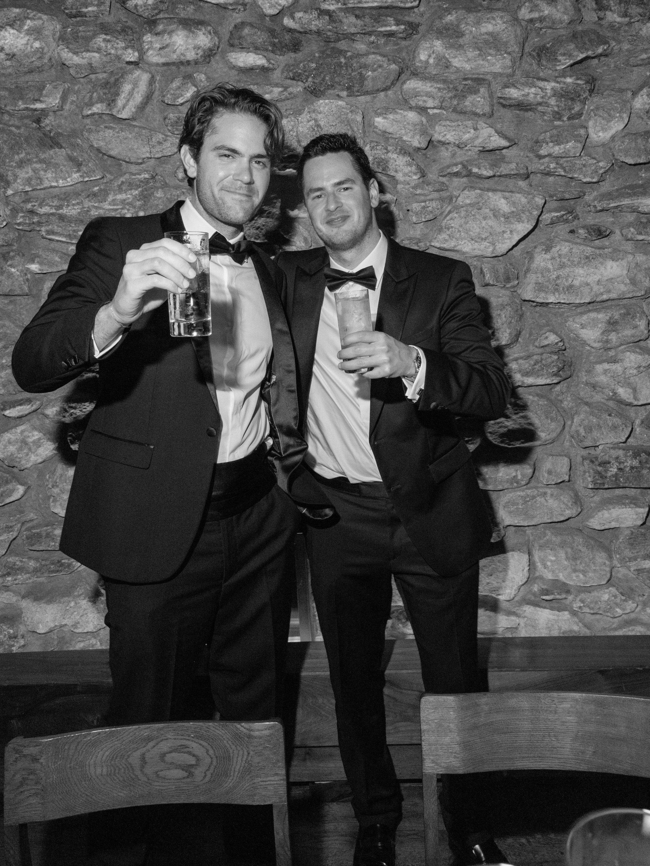 Black-and-white candid of two wedding guests raising drinks during Jennie and Will’s Blue Hill at Stone Barns reception.