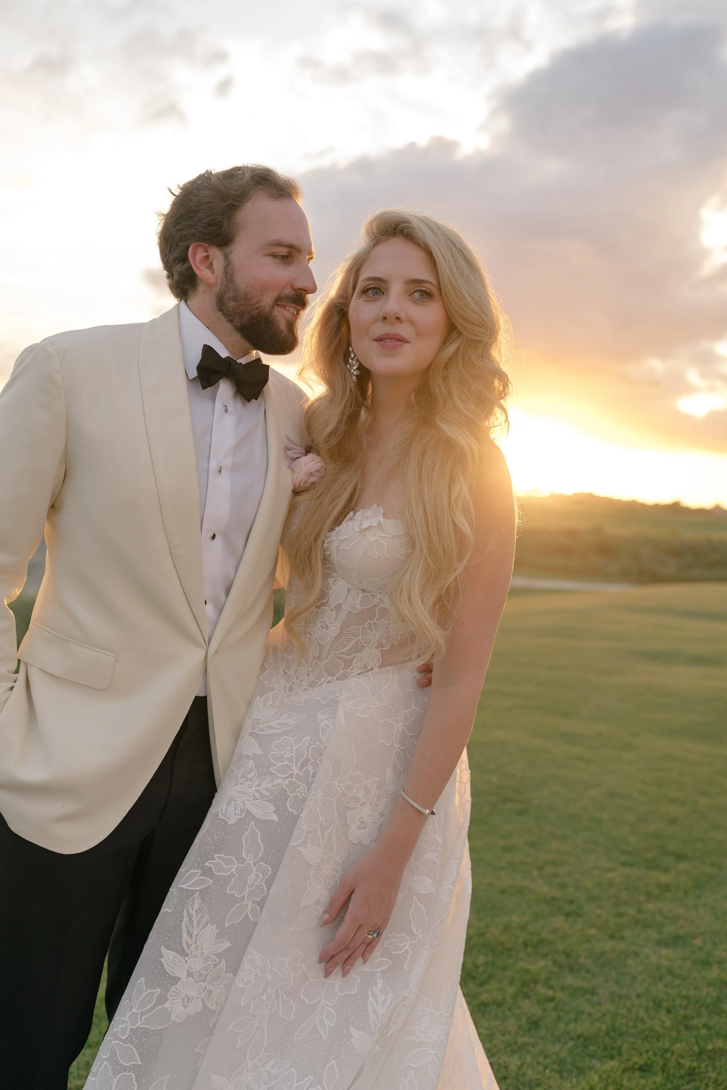 Katie and Trevor stand together in warm sunset light overlooking the Ocean Course landscape