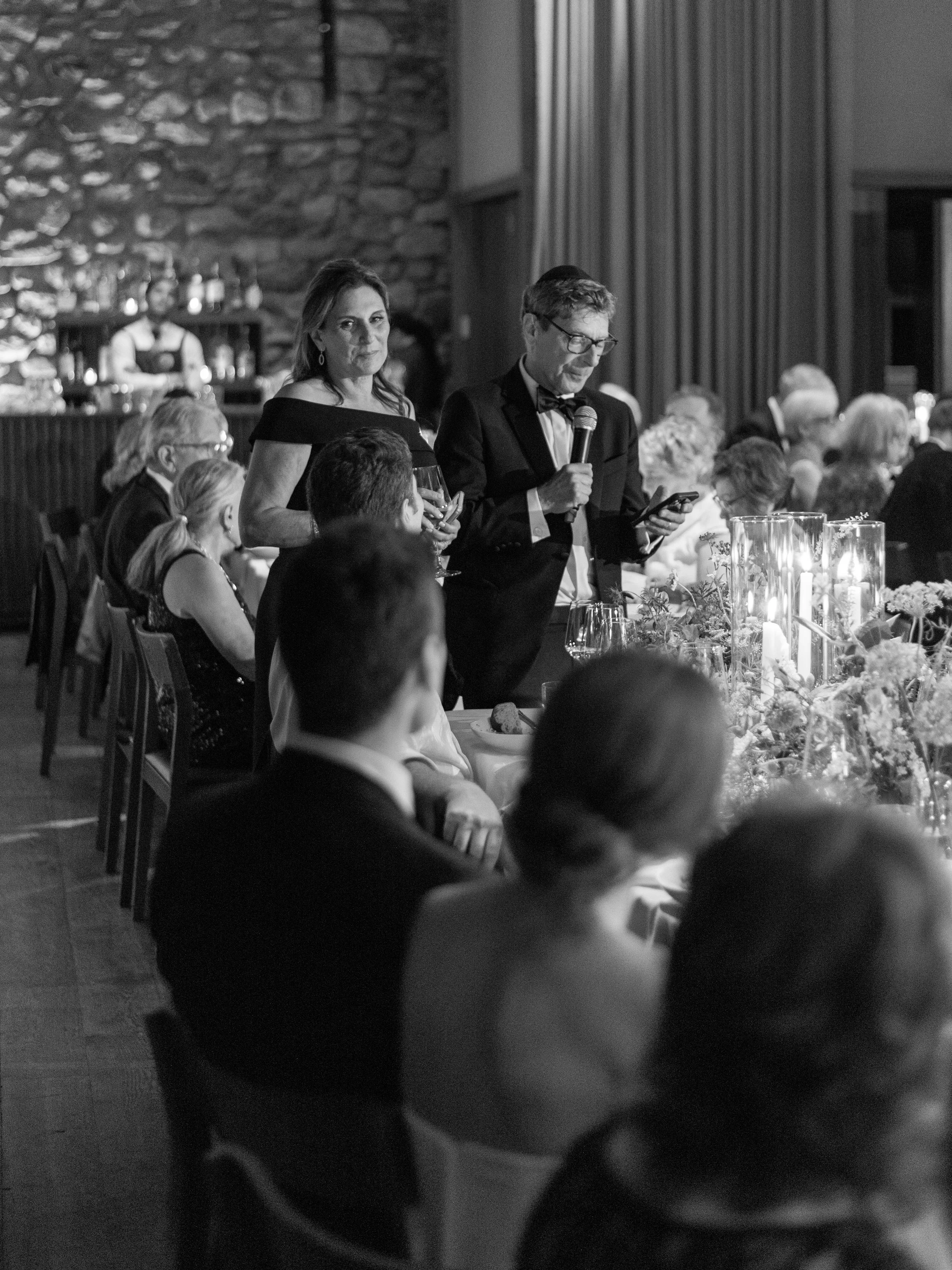 Black-and-white documentary photograph of guests listening during the wedding dinner speeches.