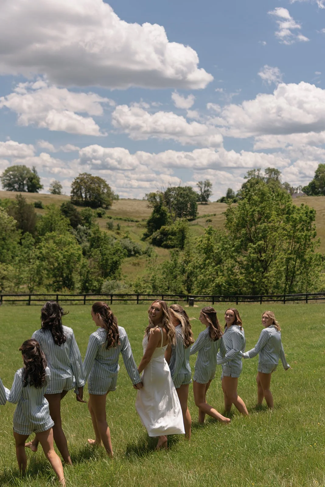 Bride and bridesmaids walking together through the spring countryside at Goodstone Inn beneath a blue sky.
