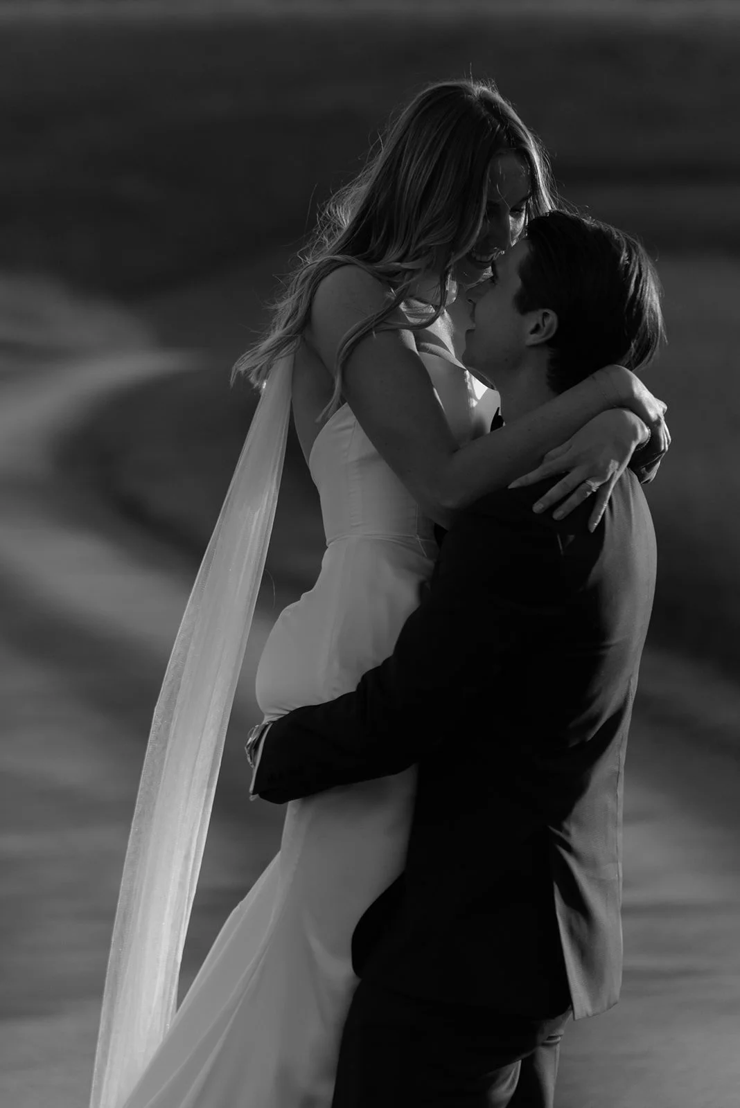 Black-and-white portrait of the groom lifting the bride during sunset golden hour
