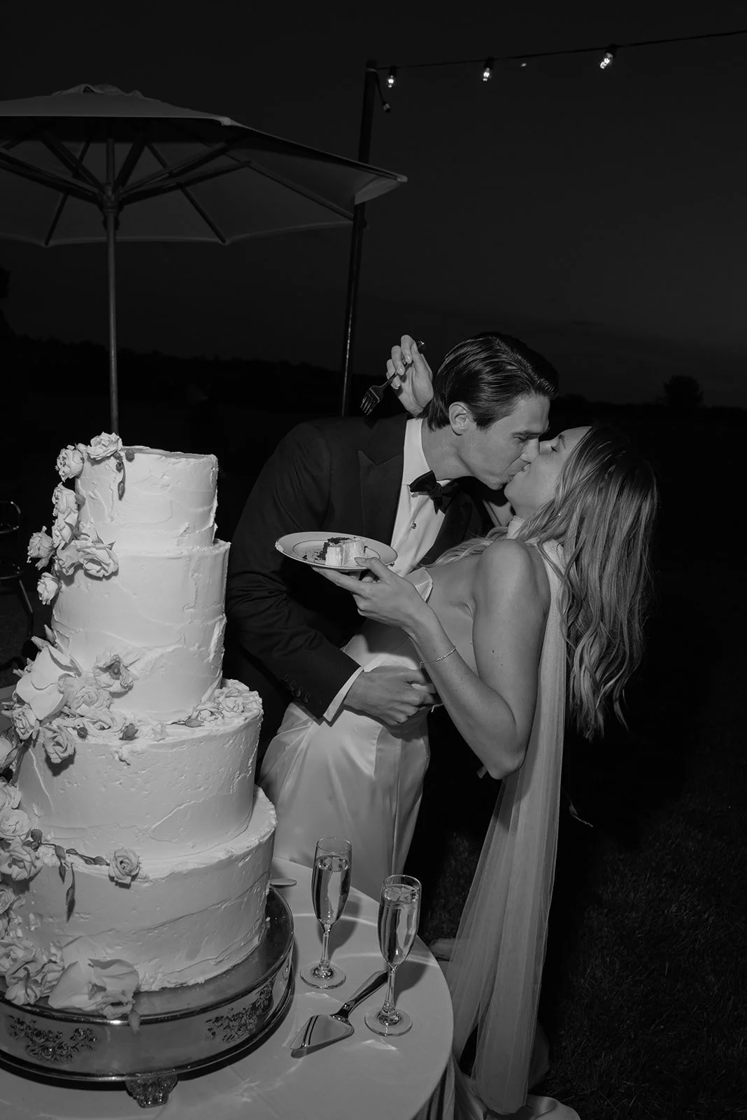 Black-and-white photograph of the bride and groom cutting their cake together during their outdoor Goodstone Inn reception.