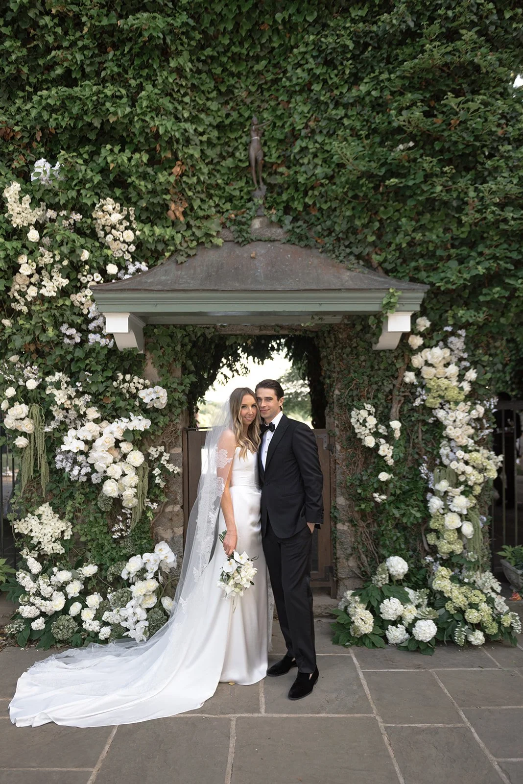 Bride and groom standing beneath the floral Ivy Wall arbor at Goodstone Inn after their ceremony.