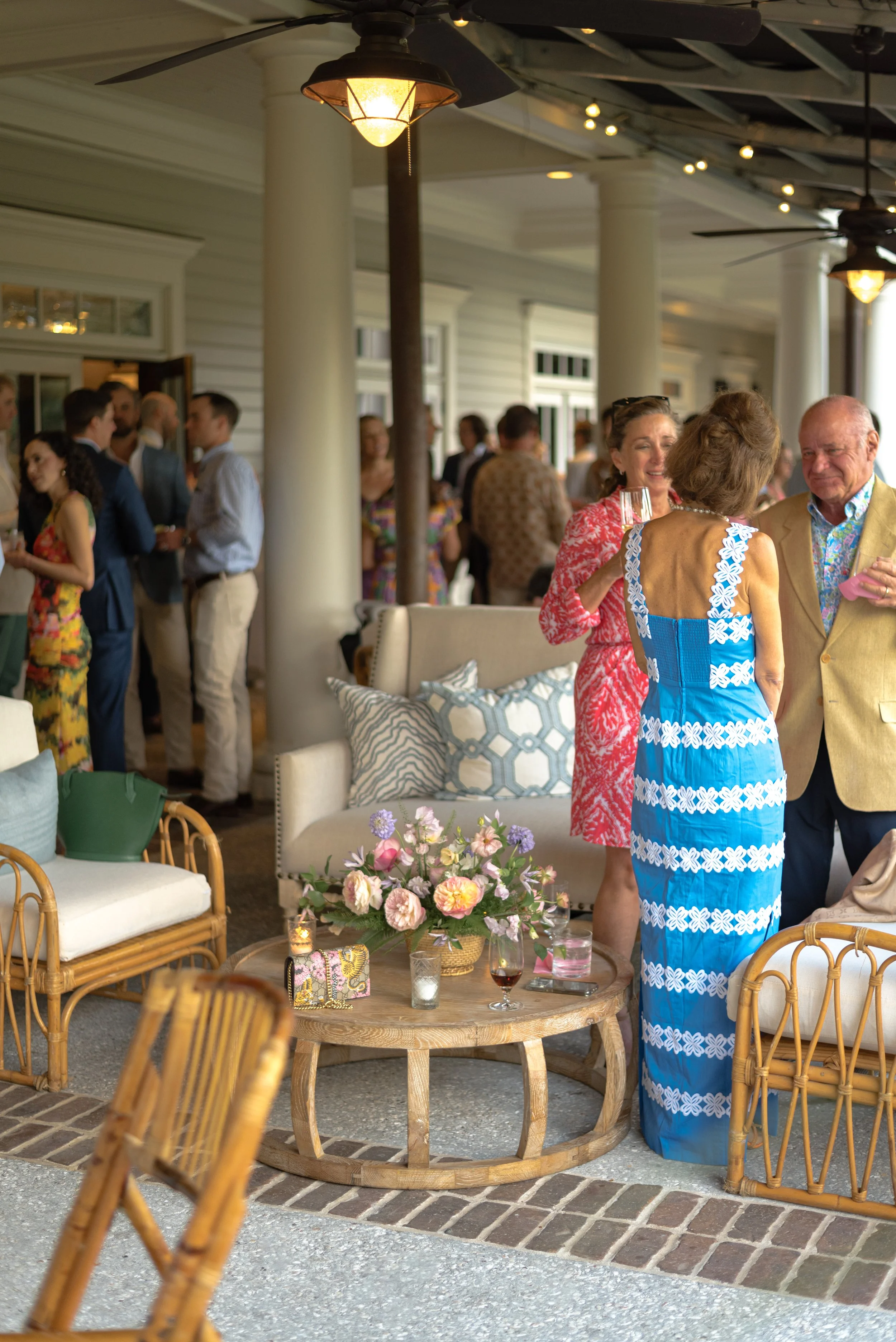 Guests in colorful evening attire mingle among rattan lounge furniture and floral arrangements at Turtle Point Clubhouse on Kiawah Island.
