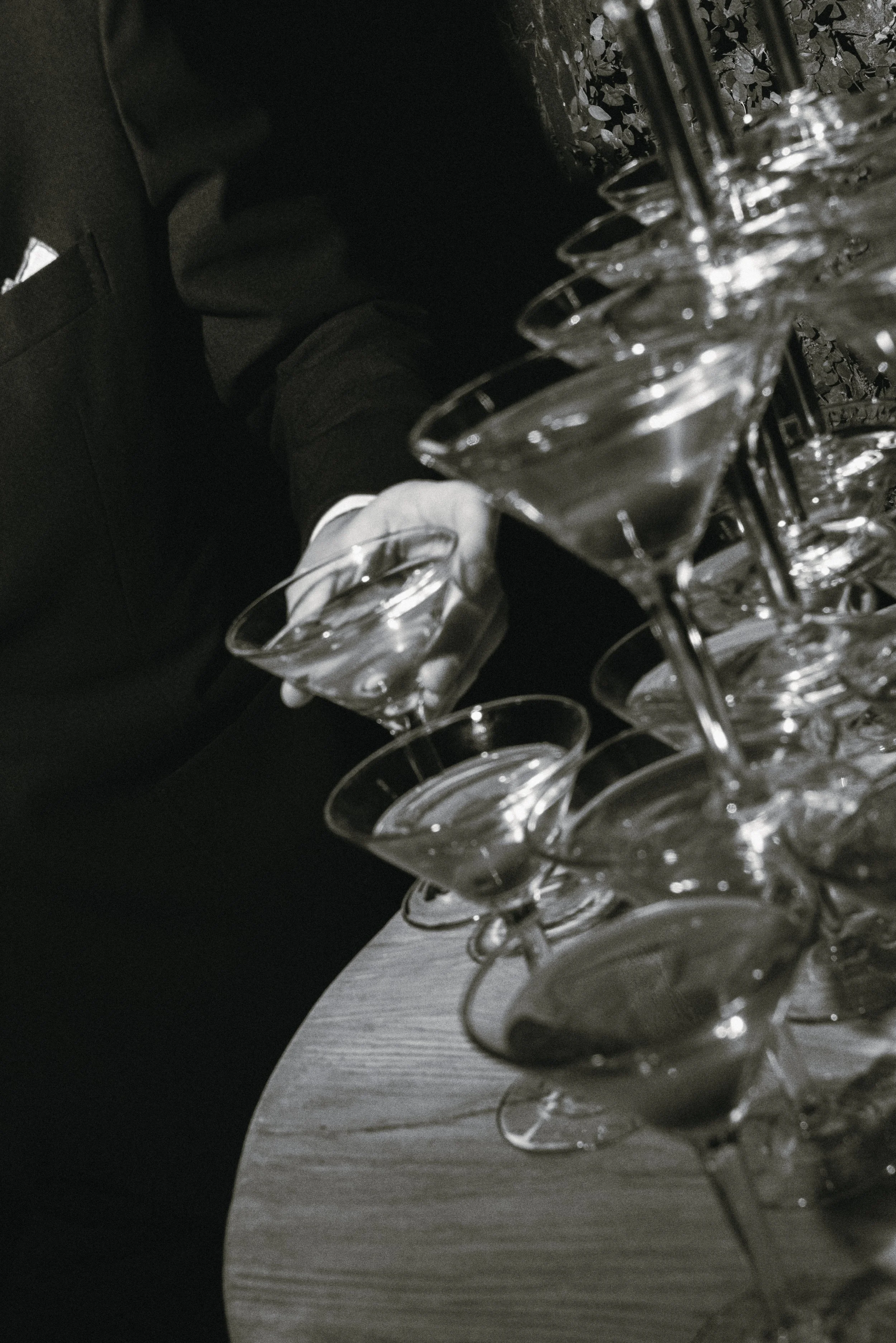 Black and white editorial photograph of champagne glasses at a wedding celebration, highlighting elegant details and the atmosphere of gathering.