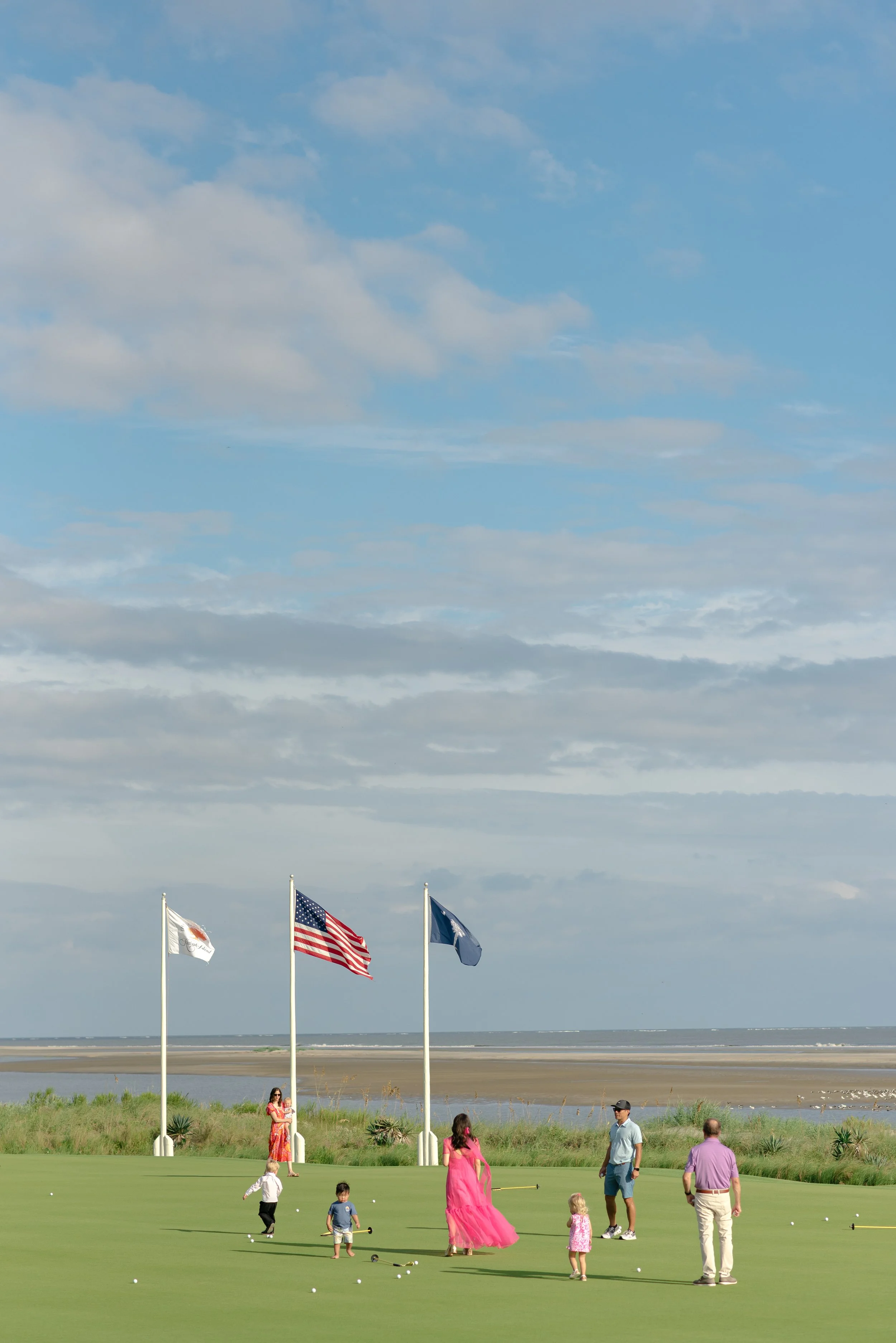 Guests cross the coastal lawn beneath flags at The Ocean Course while the wedding spaces are prepared before the ceremony.