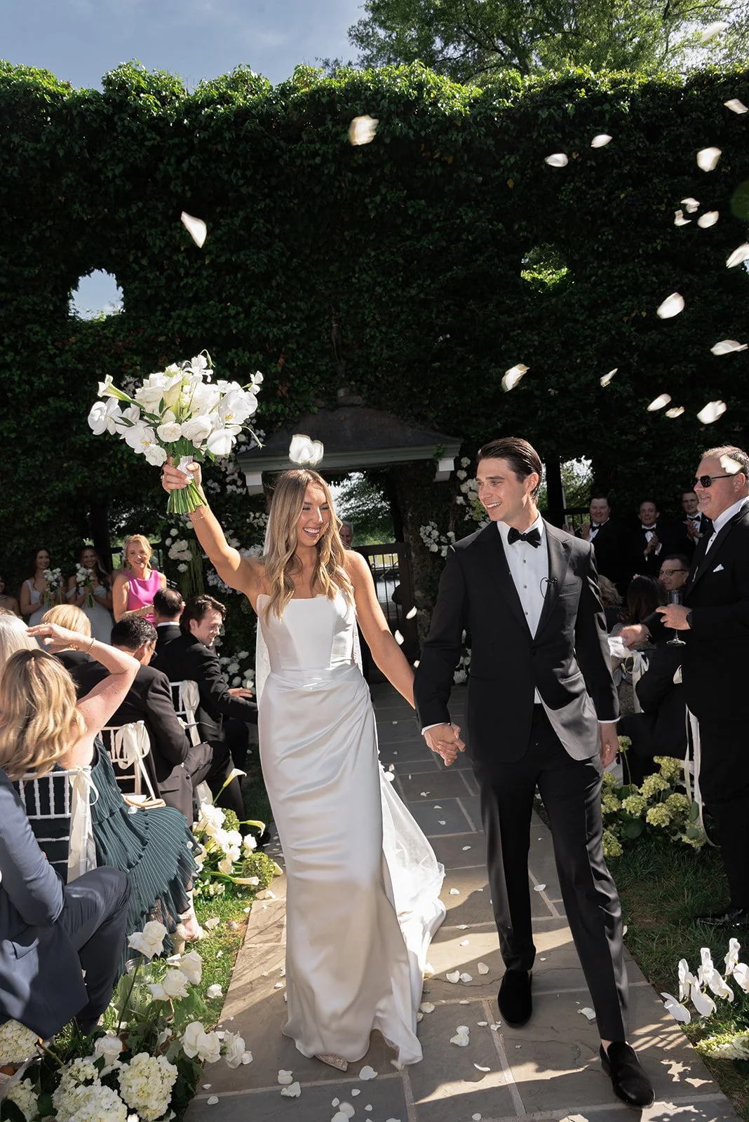 Newlyweds walking through the garden ceremony aisle as guests toss rose petals at Goodstone Inn.