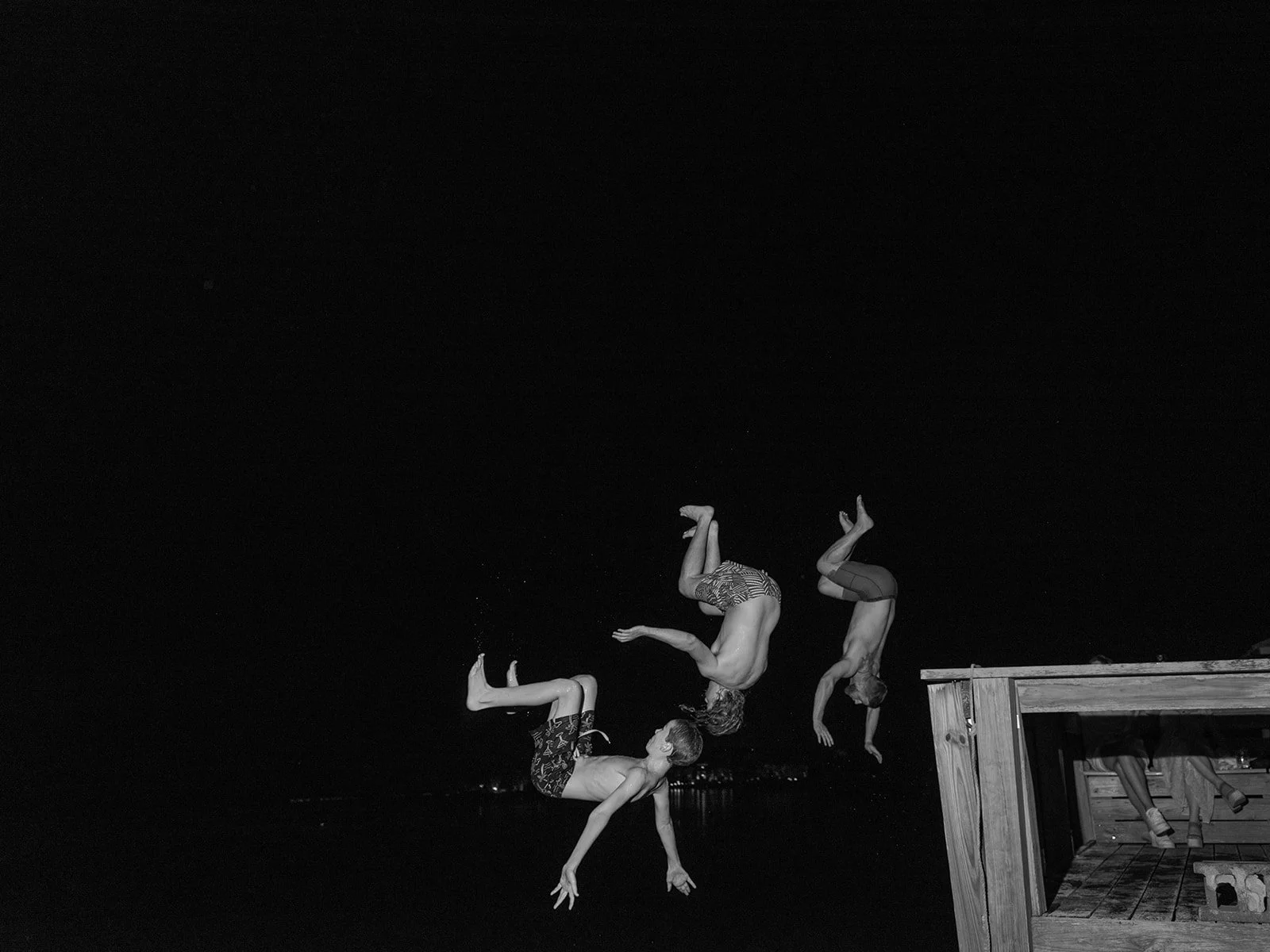Black and white photograph of children leaping from a dock into the ocean during a seaside wedding celebration in Murrells Inlet, South Carolina, capturing an unexpected and joyful moment beyond the traditional wedding day.