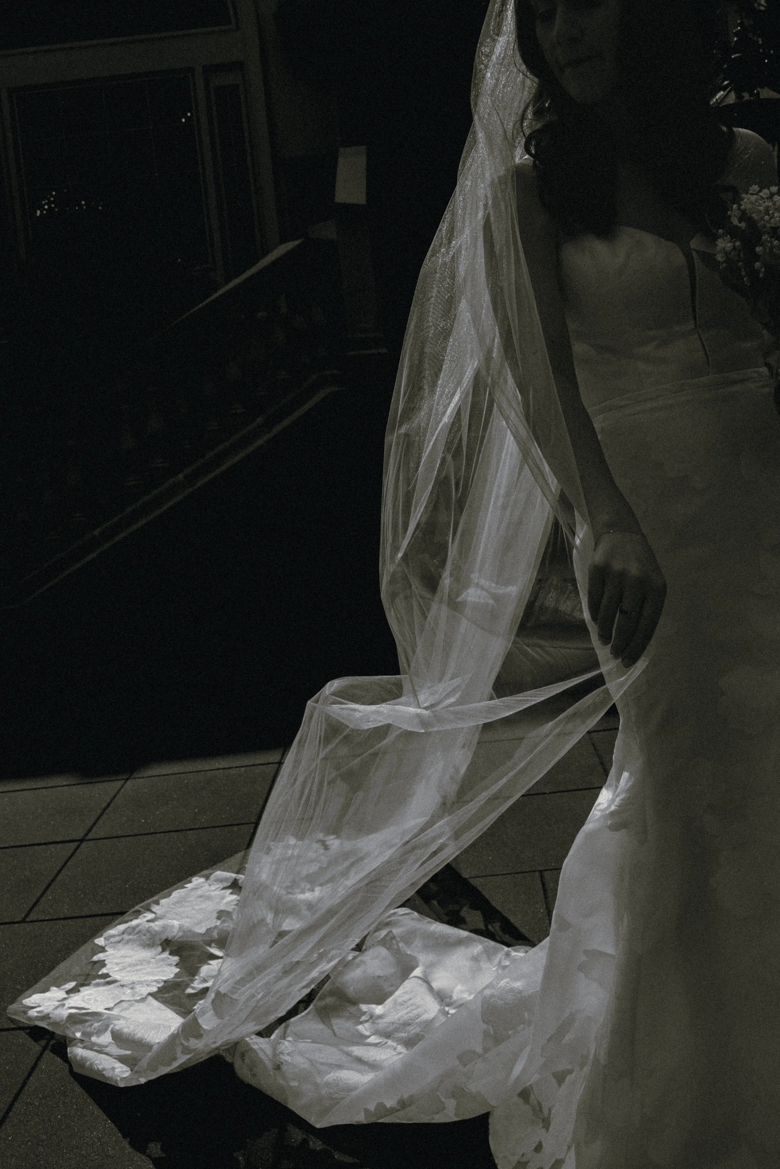 Long bridal veil hanging off the bride in dramatic shadow before a wedding ceremony.