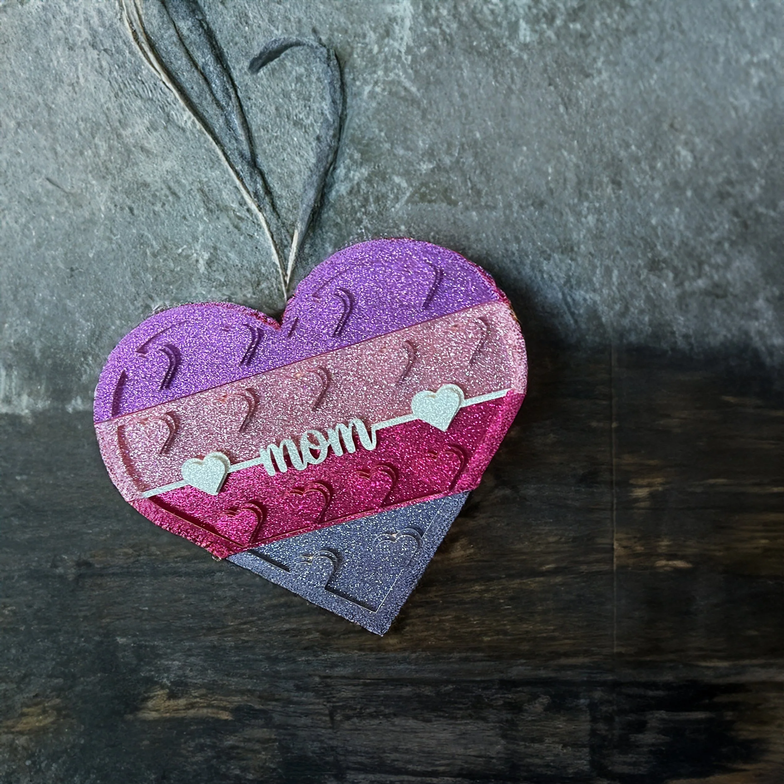 Colorful heart-shaped foam decoration with the word 'mom' and small hearts on it, placed on a dark surface.