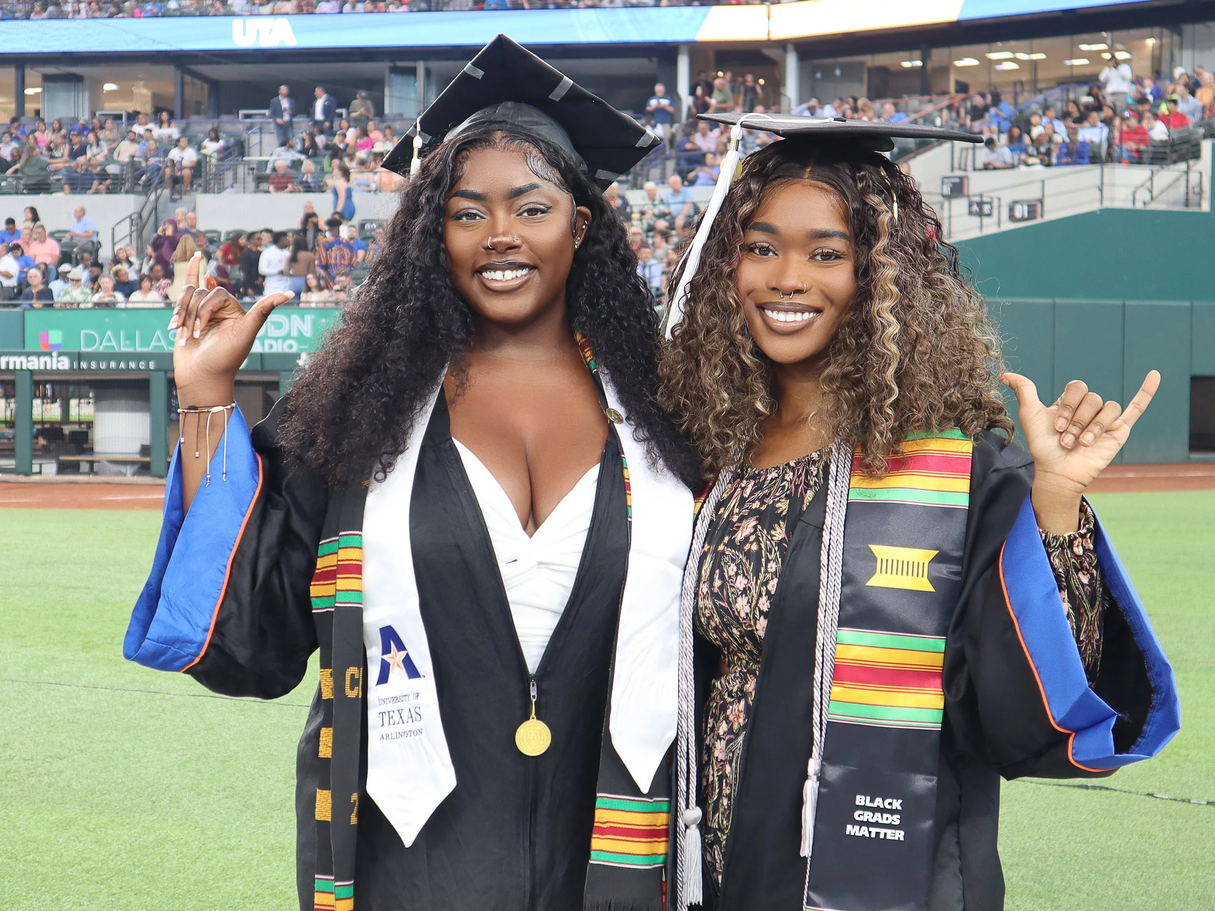 Two female students in their graduation cap and gown smiling for a picture